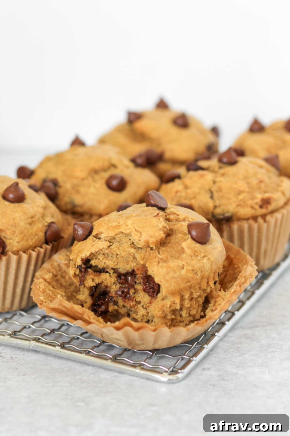 A delicious banana protein muffin with a bite taken out, revealing its fluffy texture and chocolate chips, with other muffins in the background.