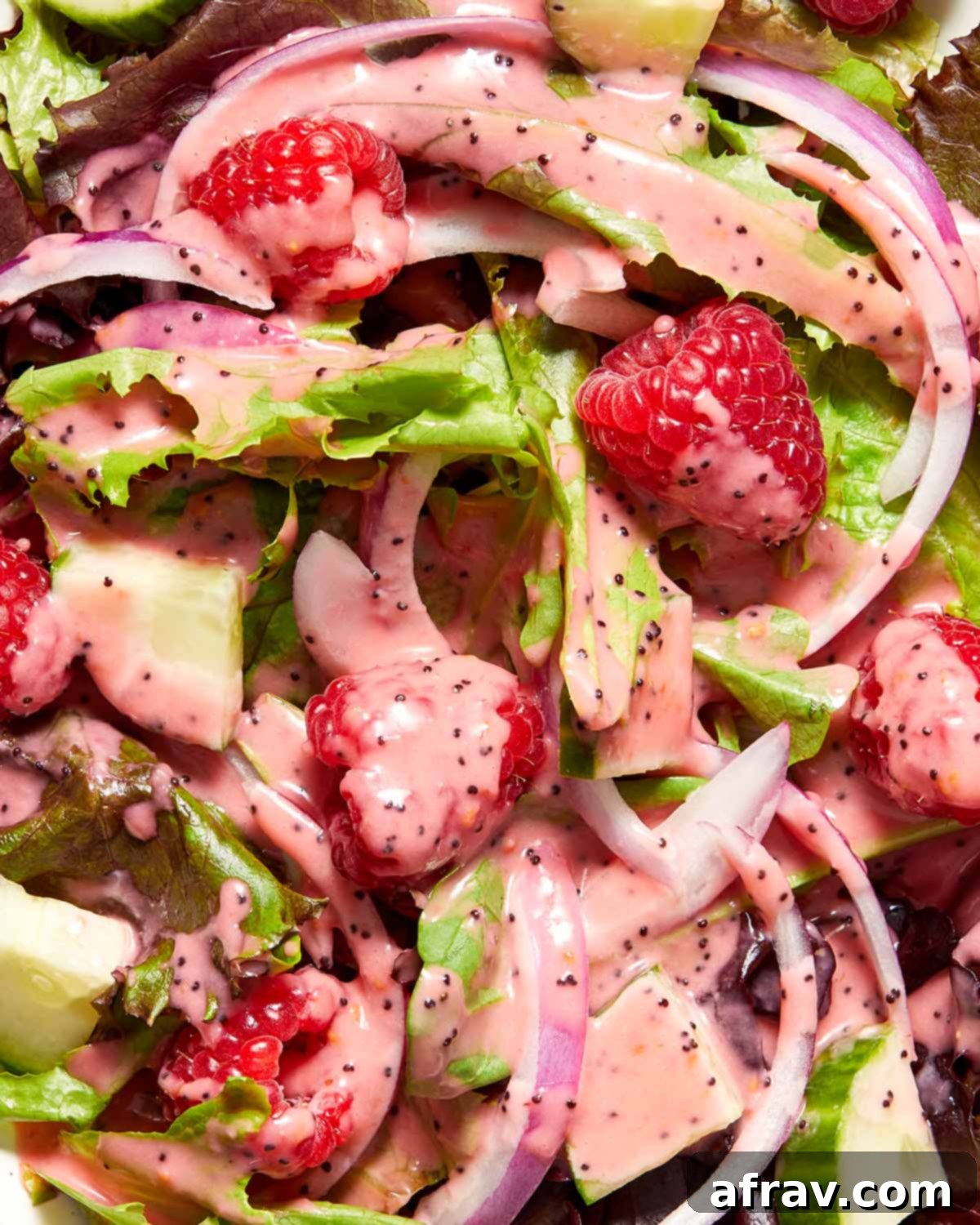 Close up overhead view of vibrant red raspberry dressing generously drizzled over a fresh green salad, with visible poppy seeds and whole raspberries scattered on top.