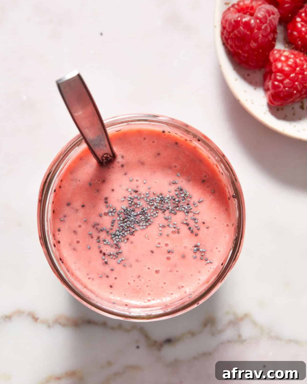 Overhead view of homemade raspberry poppy seed dressing in a glass jar, with poppy seeds visible and a vibrant pink hue, ready for use.
