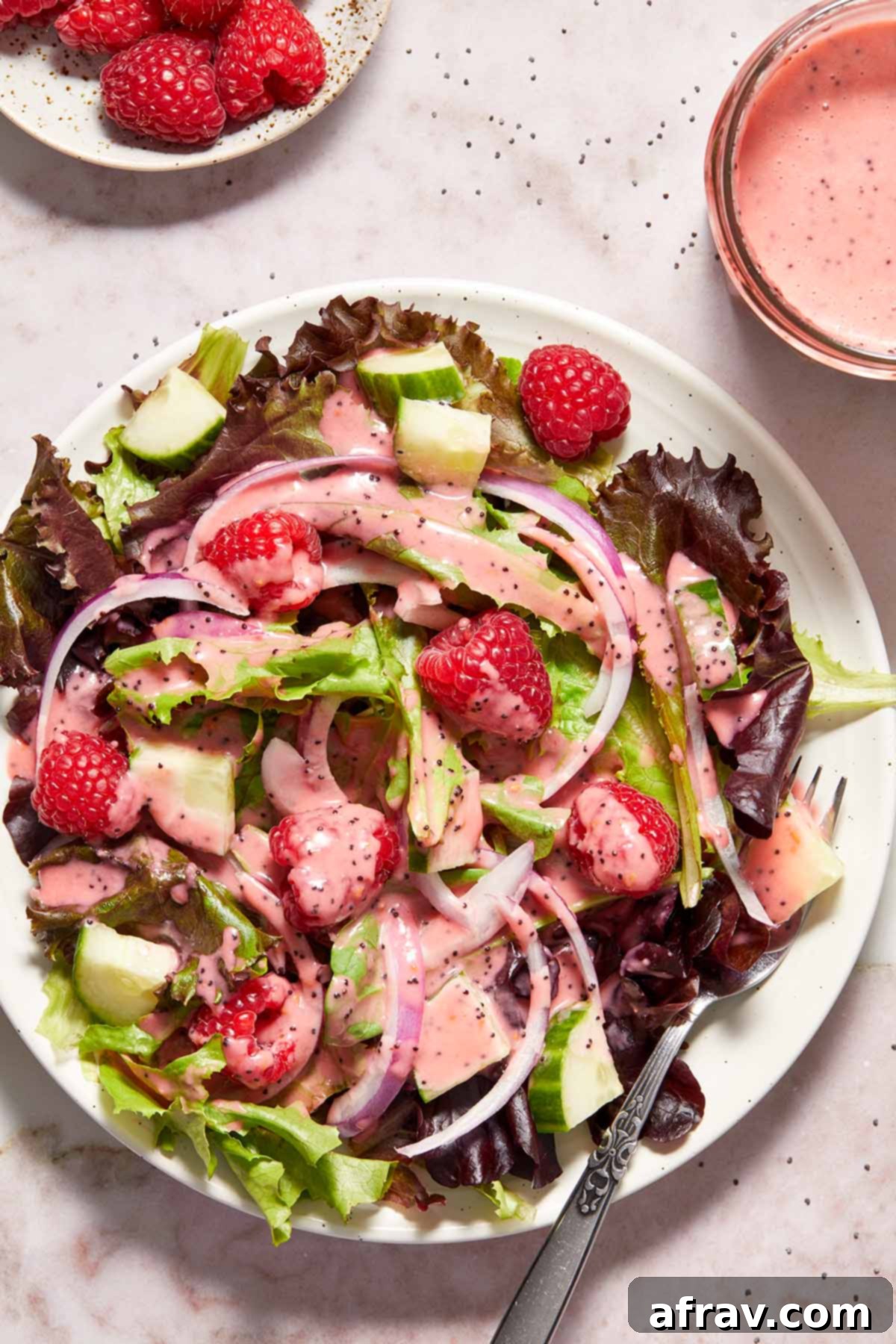 A crisp green salad on a white plate, elegantly dressed with a drizzle of homemade raspberry poppy seed dressing and garnished with fresh raspberries.