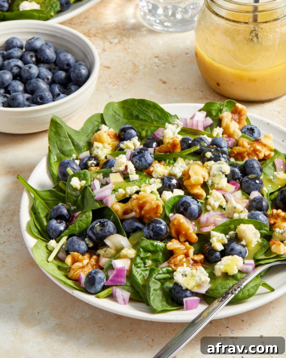 Angled view of blueberry salad on a white plate with blueberries and dijon dressing in the background.