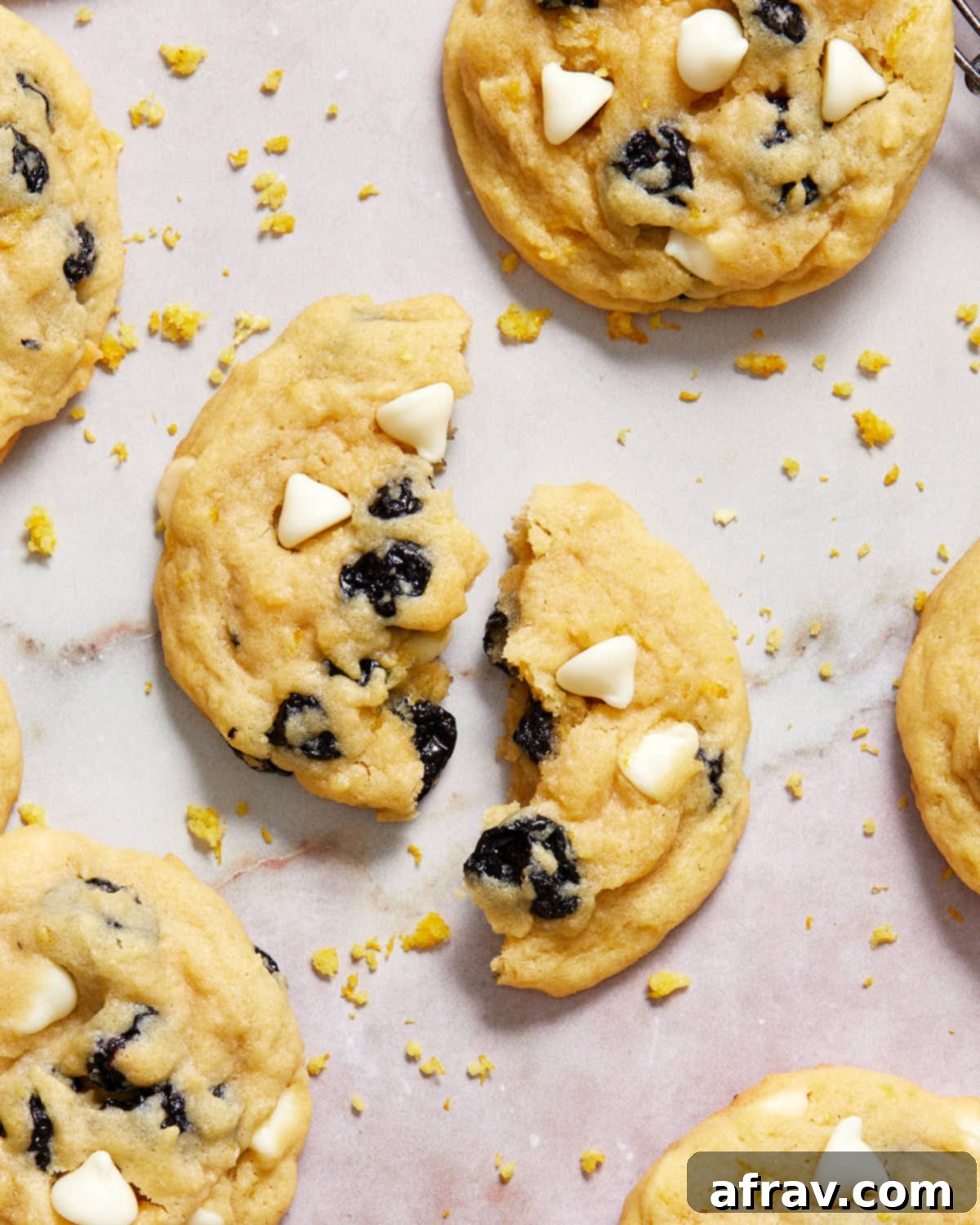 Overhead view of a lemon blueberry cookie broken in half, revealing its soft interior, juicy blueberries, and melted white chocolate chips.