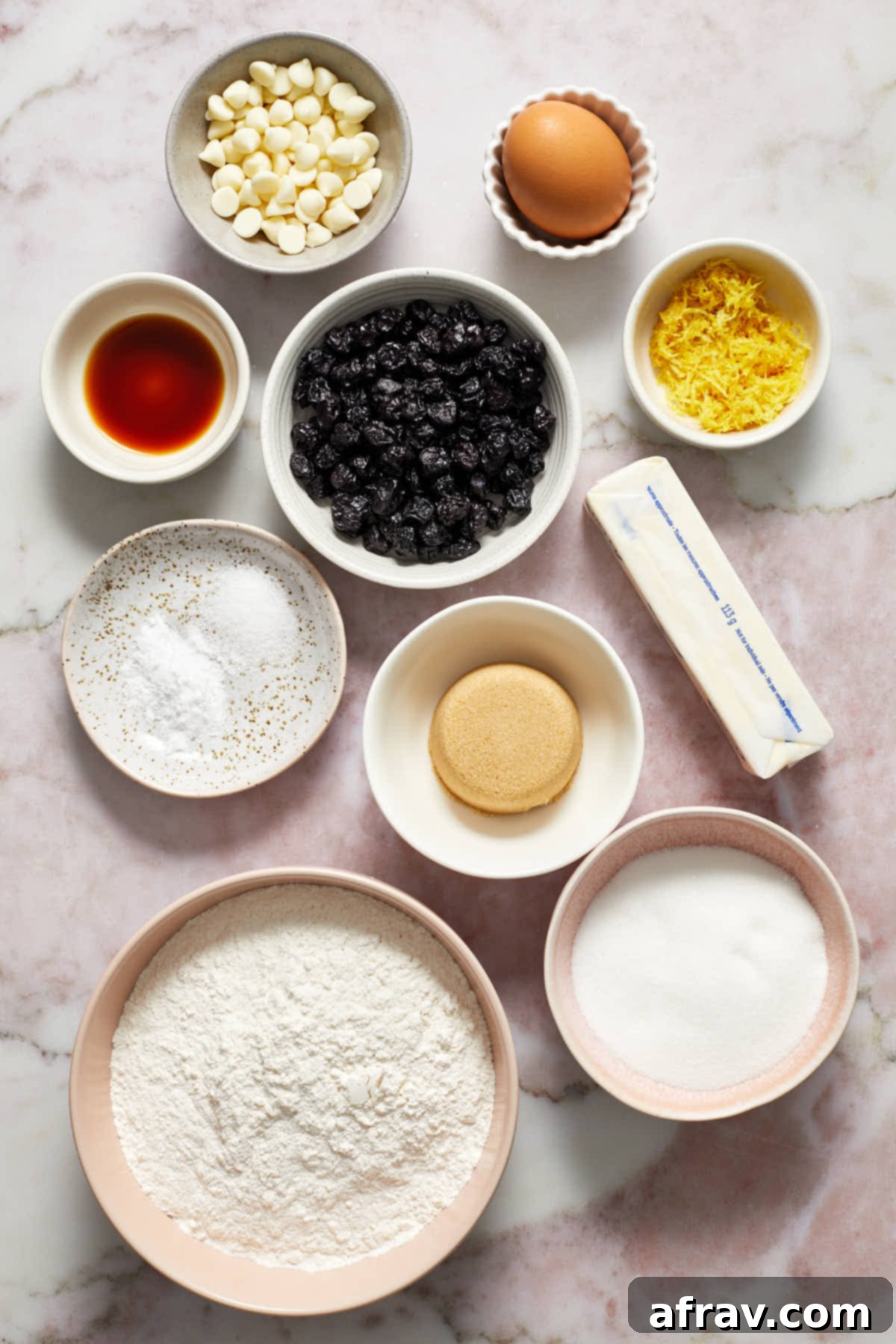 Various ingredients for blueberry lemon cookies, including flour, sugar, butter, lemons, blueberries, and white chocolate chips, neatly arranged.