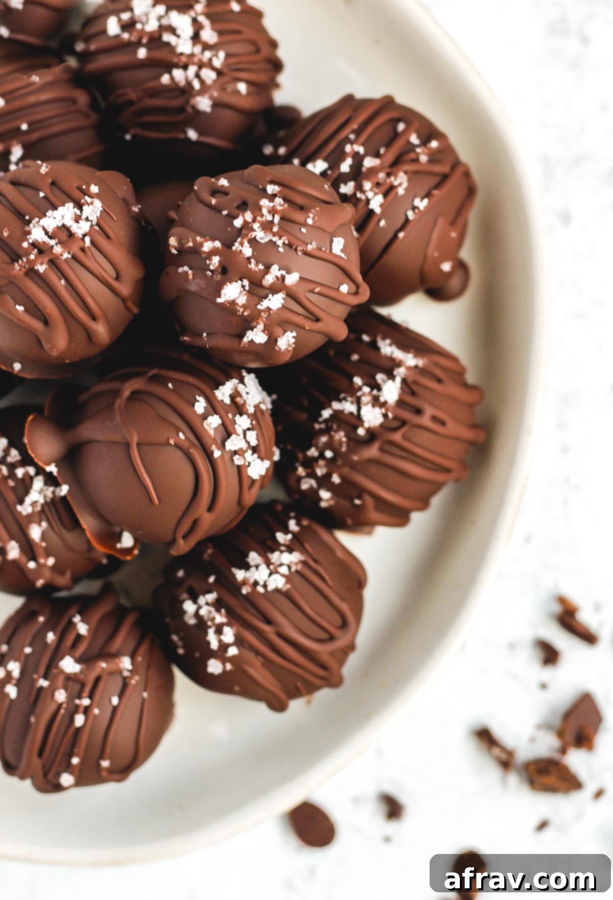 Two healthy chocolate covered peanut butter balls, drizzled with chocolate and sea salt, stacked on a simple white plate.