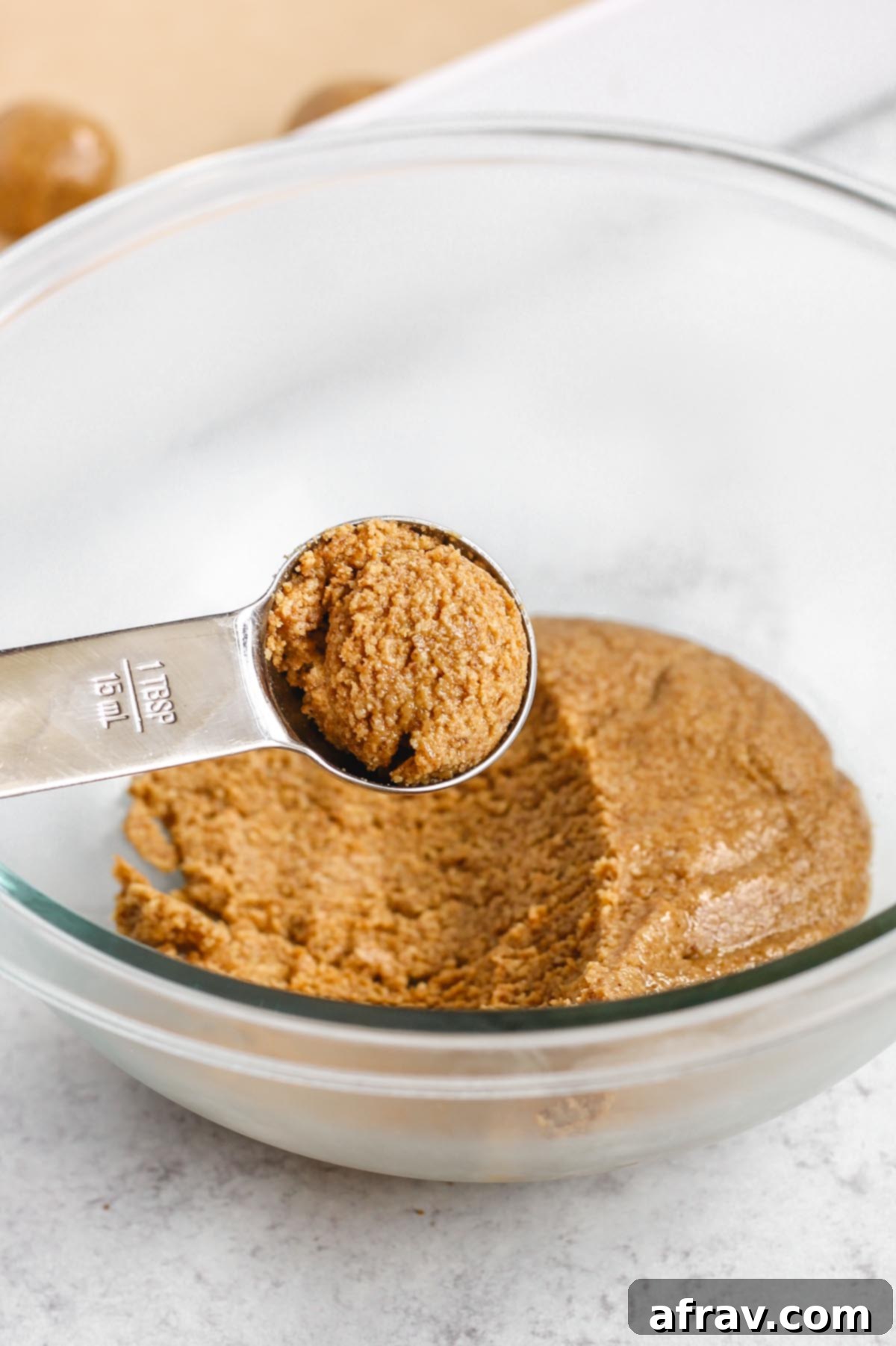 A scoop of peanut butter dough being taken from the bowl with a small cookie scoop.