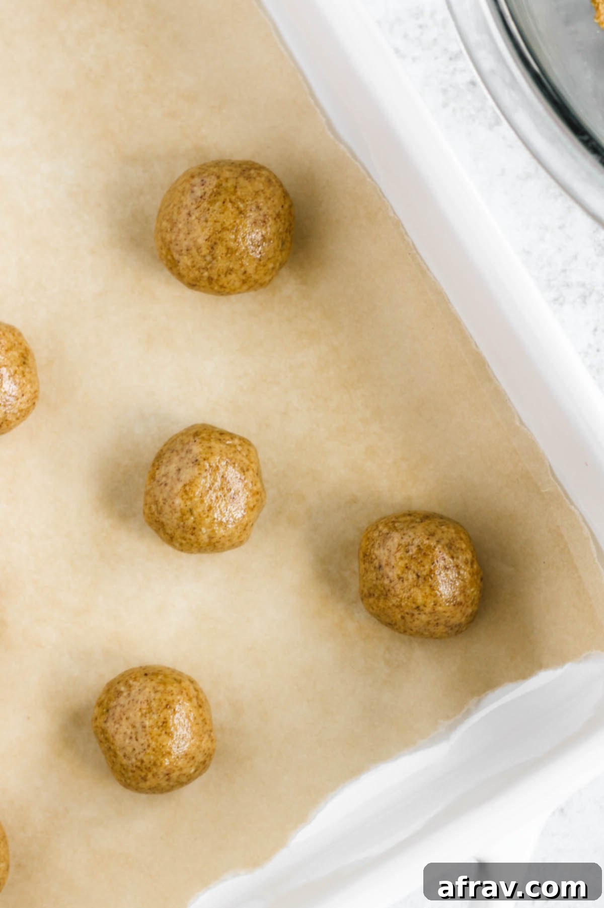 Neatly rolled peanut butter dough balls arranged in a white baking dish lined with parchment paper.