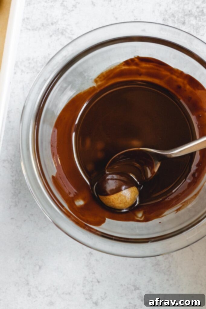 A peanut butter ball being carefully rolled in rich, melted dark chocolate using a spoon.