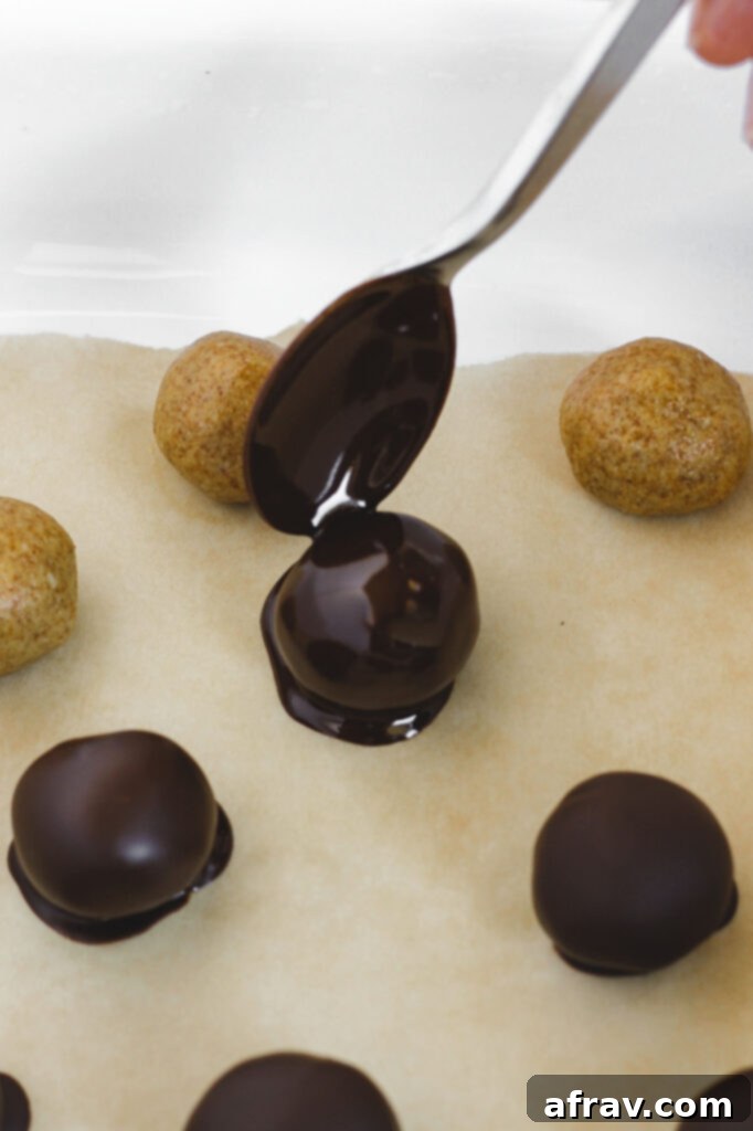 A freshly chocolate covered peanut butter ball being placed gently onto parchment paper to set.