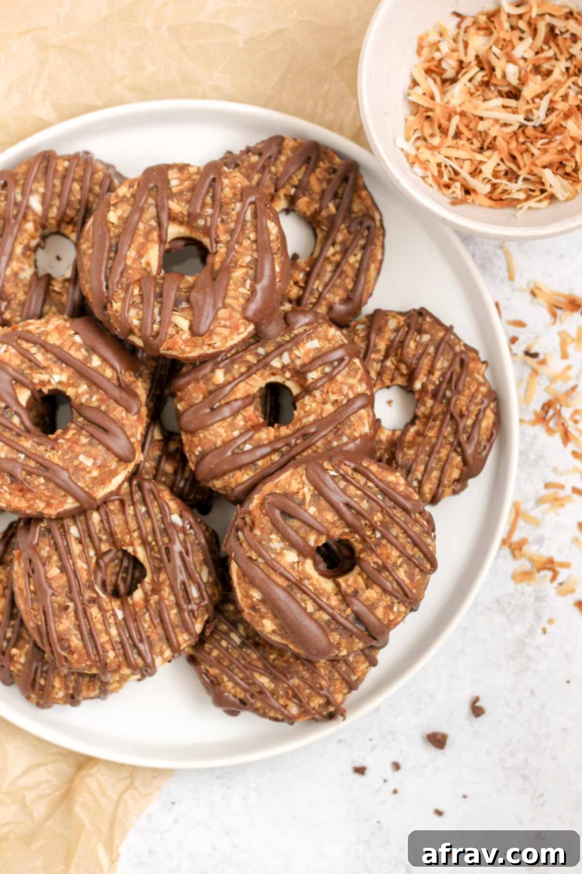 A plate of homemade Samoa cookies next to a small bowl of toasted shredded coconut, highlighting the dessert's main components.