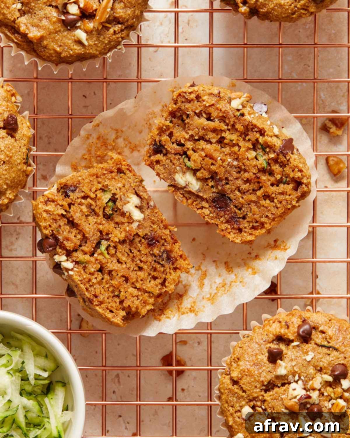 Overhead view of a zucchini muffin cut in half on a parchment paper wrapper on a wire rack.