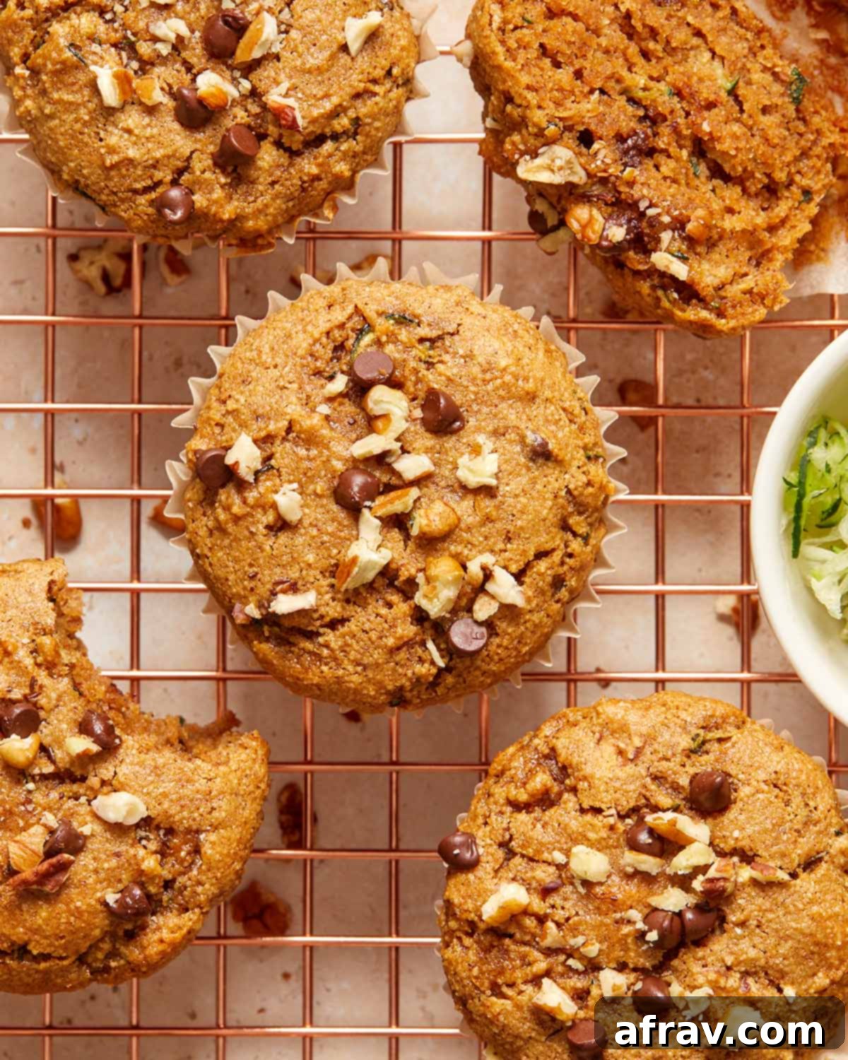 Zucchini muffins topped with chocolate chips and pecans and cooling on a wire rack.