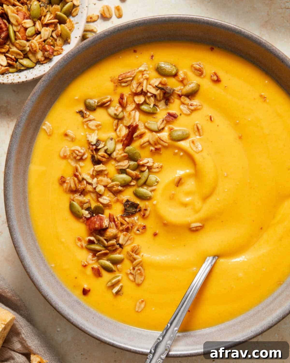 Close up of carrot butternut squash soup in a bowl and topped with savory granola.