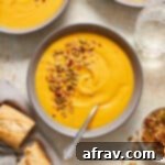 A bowl of carrot and butternut squash soup topped with savory granola next to some crusty bread.