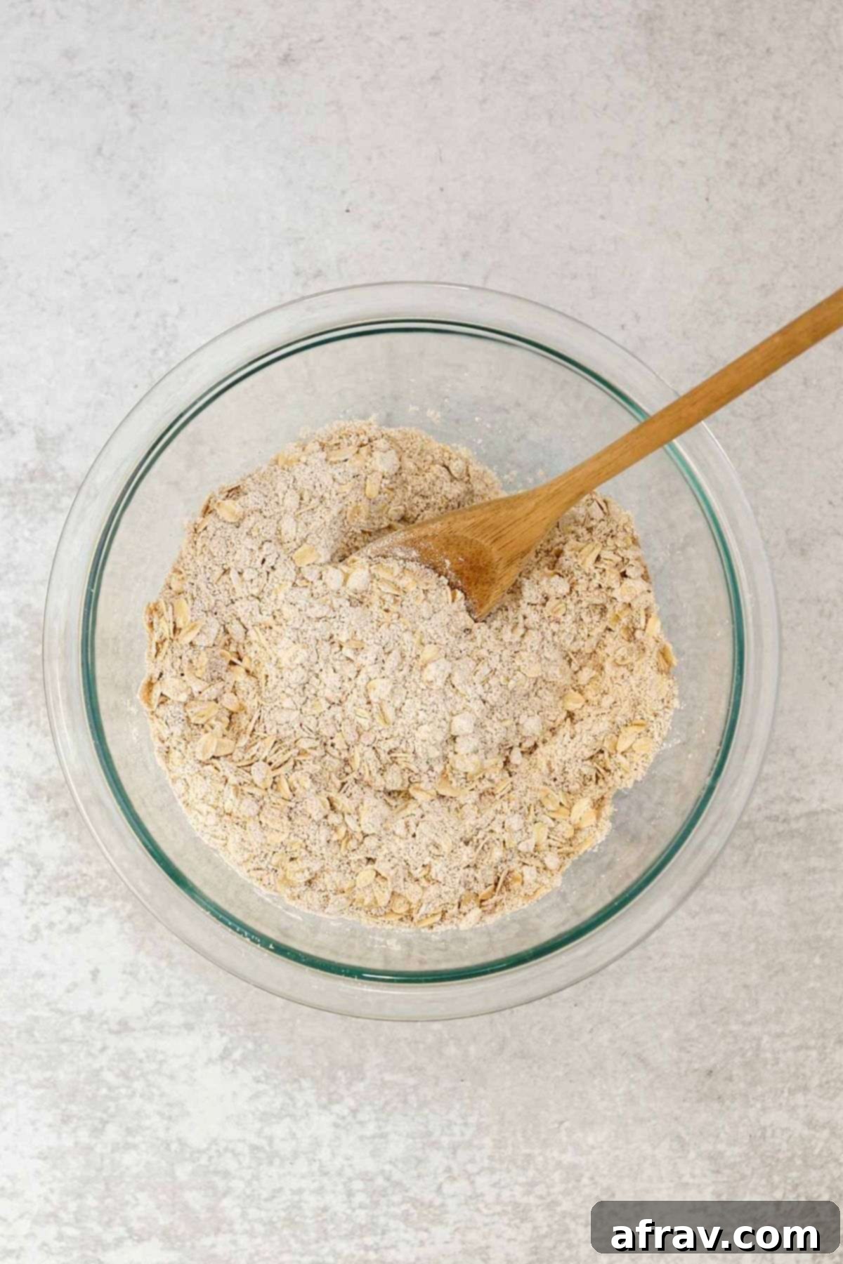 Spiced Carrot Oatmeal Delights 4 Dry ingredients needed for carrot cake oatmeal cookies in a glass mixing bowl with a wooden spoon.