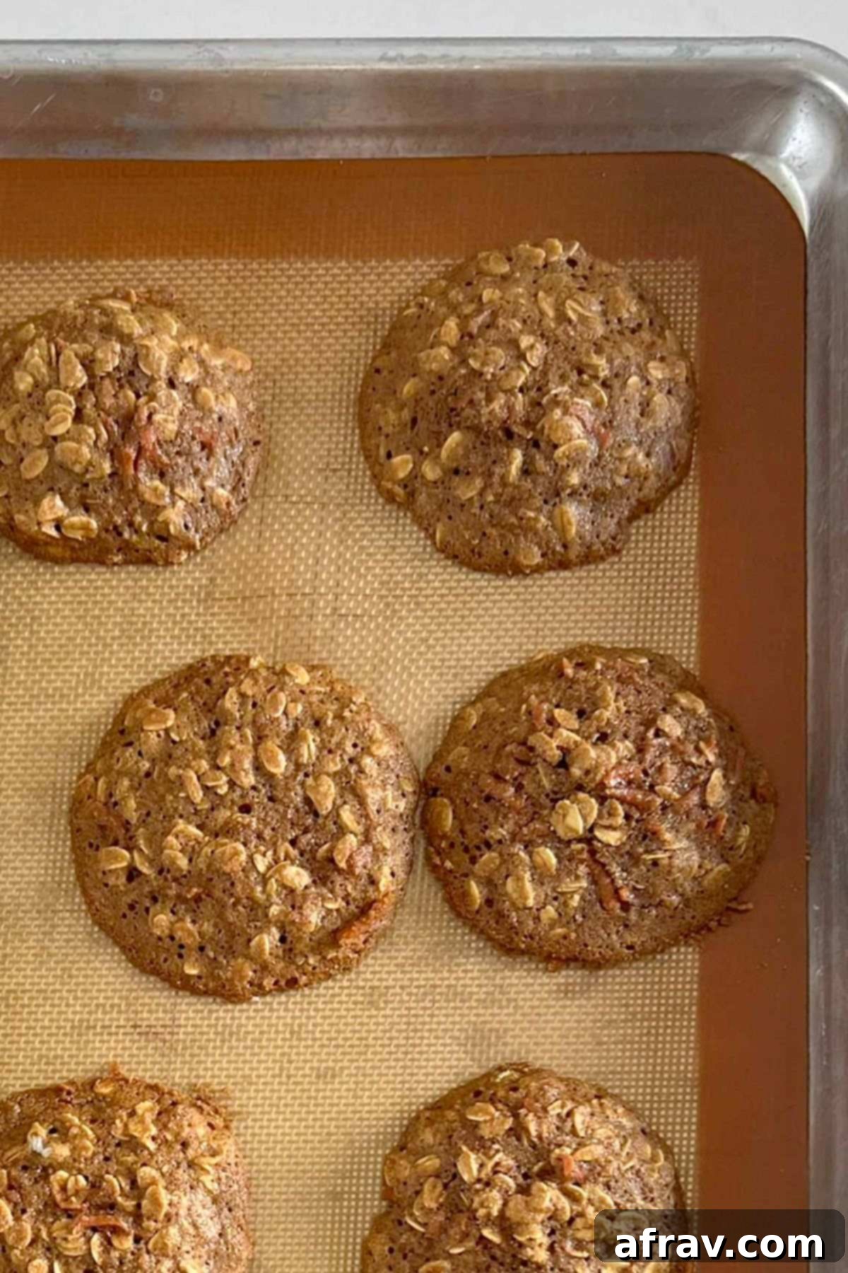 Spiced Carrot Oatmeal Delights 8 Baked carrot cake oatmeal cookies on a cookie sheet.