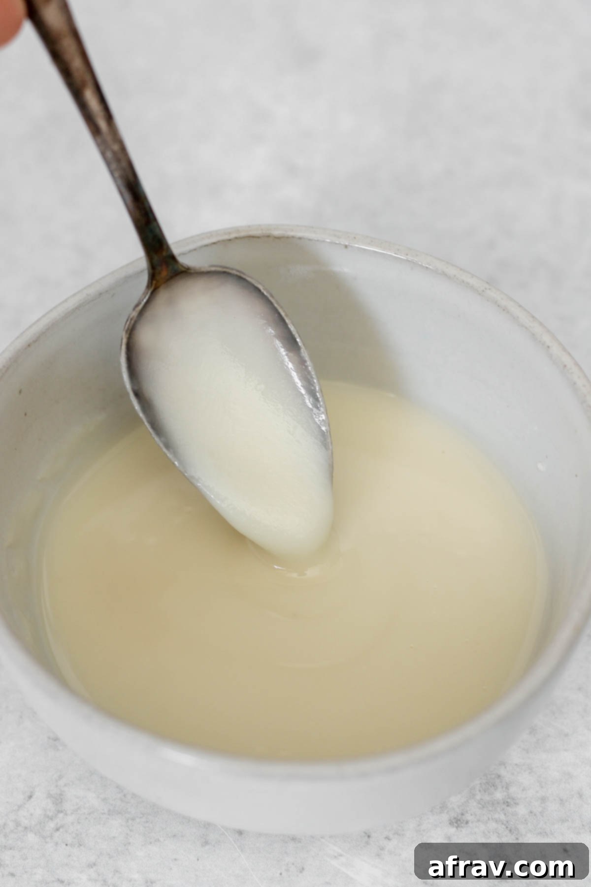 Smooth, creamy coconut butter glaze dripping from a spoon into a small ceramic bowl, showcasing its perfect drizzle consistency.