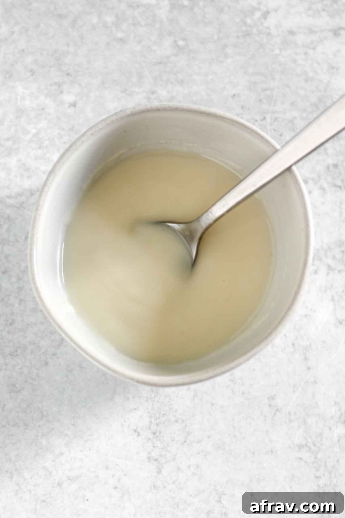 Smooth, melted coconut butter in a small bowl with a spoon, demonstrating its liquid state.