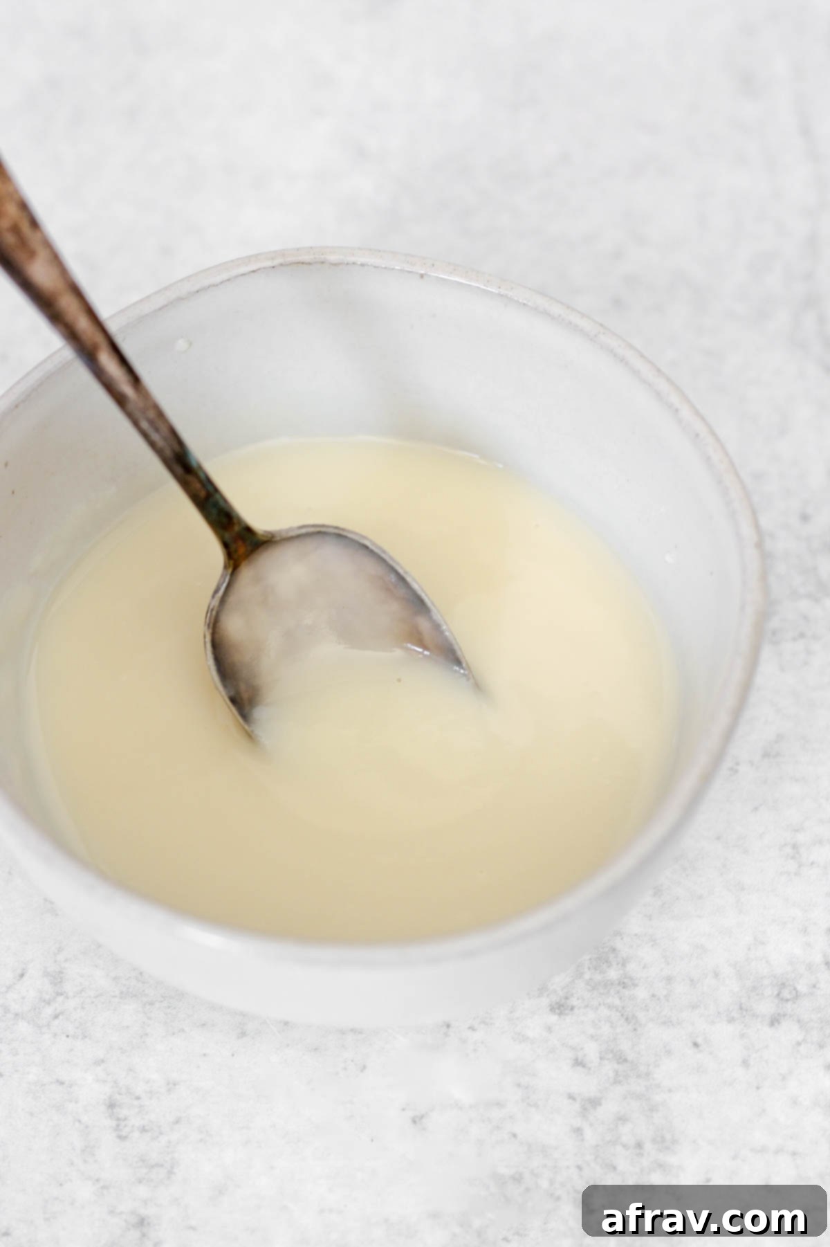 Smooth, finished coconut butter glaze in a bowl with a small spoon scooping up some glaze, showing its beautiful consistency.