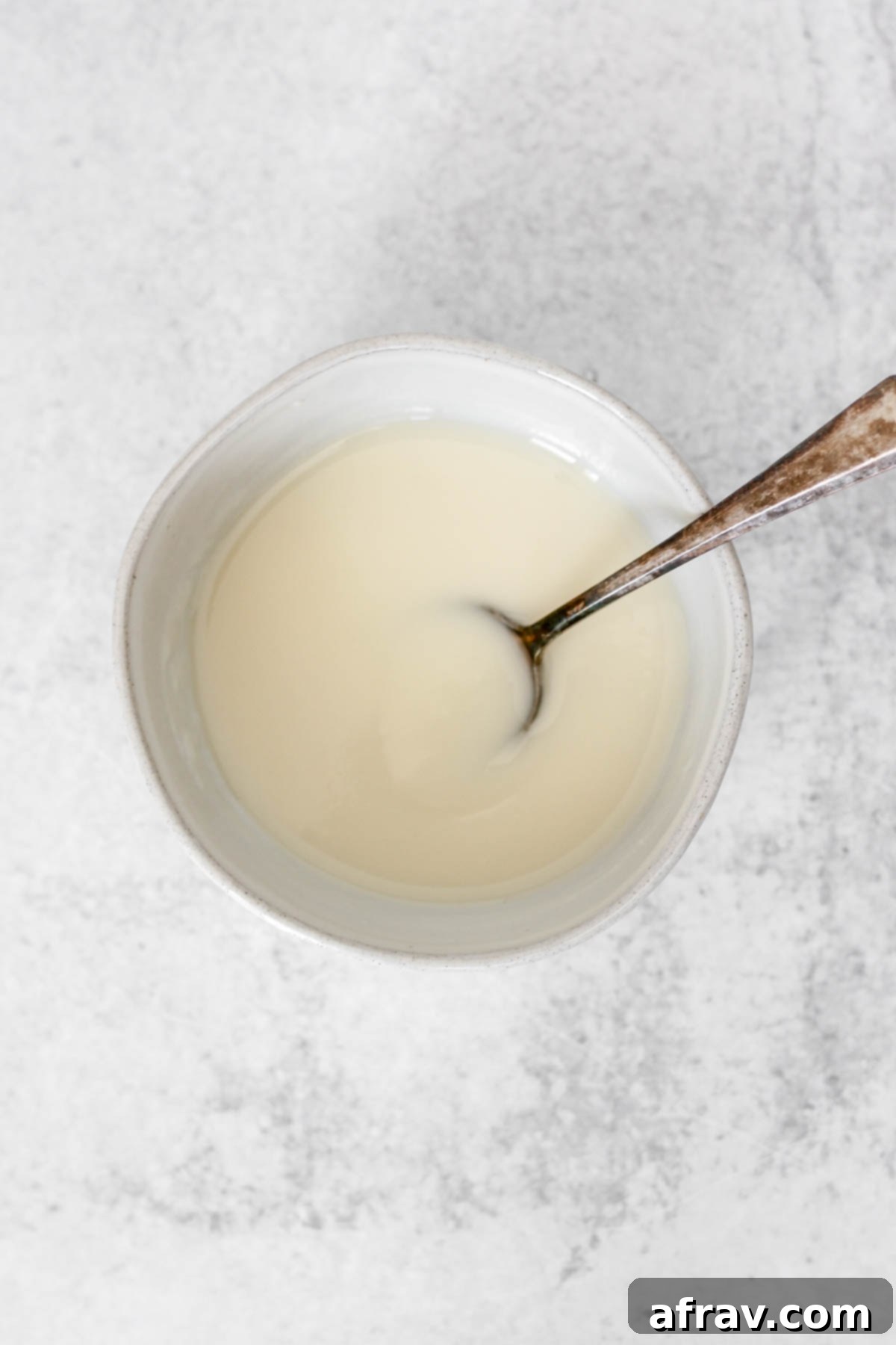 A small ceramic bowl filled with creamy coconut butter icing, with a vintage spoon resting inside, ready to be served.