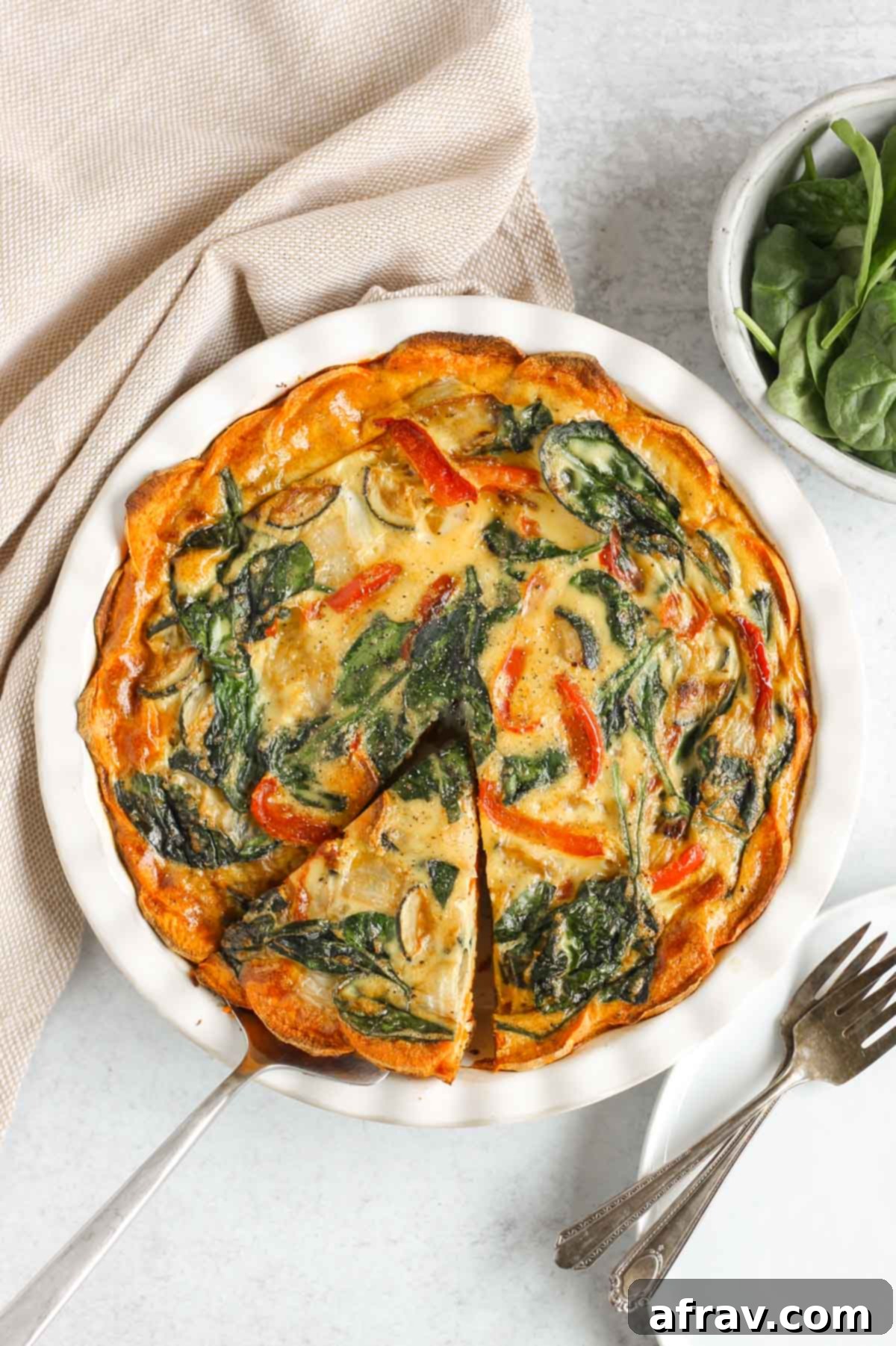 Sweet potato crust quiche with one slice cut and being served from the pie dish, showcasing its golden crust and colorful filling.