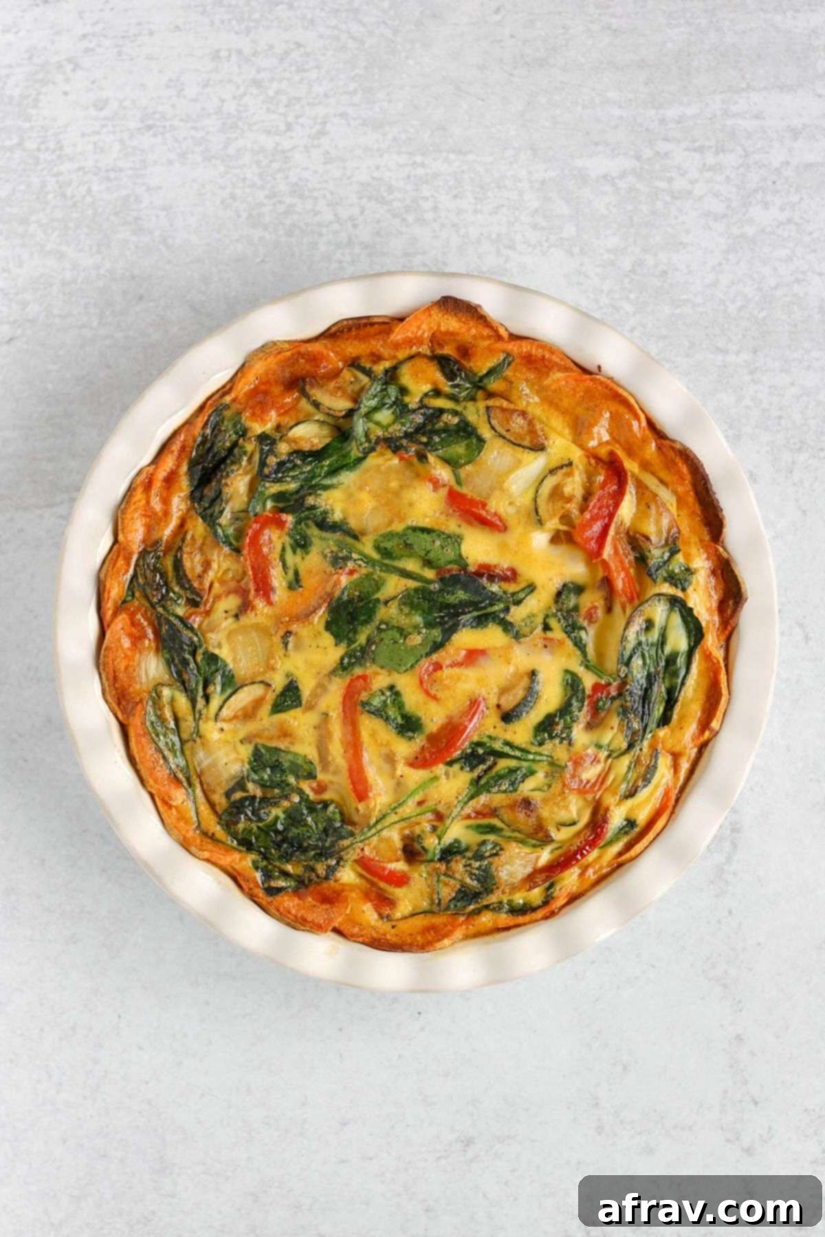 Freshly baked sweet potato crust quiche, golden brown and set, cooling in a white ceramic pie dish after being removed from the oven.