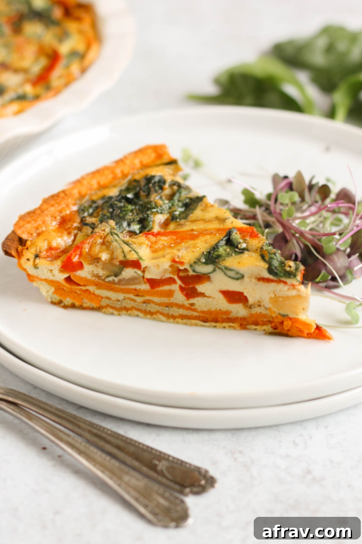 A delectable slice of sweet potato crust quiche served on two stacked white plates, accompanied by vintage silver forks, ready to be eaten.