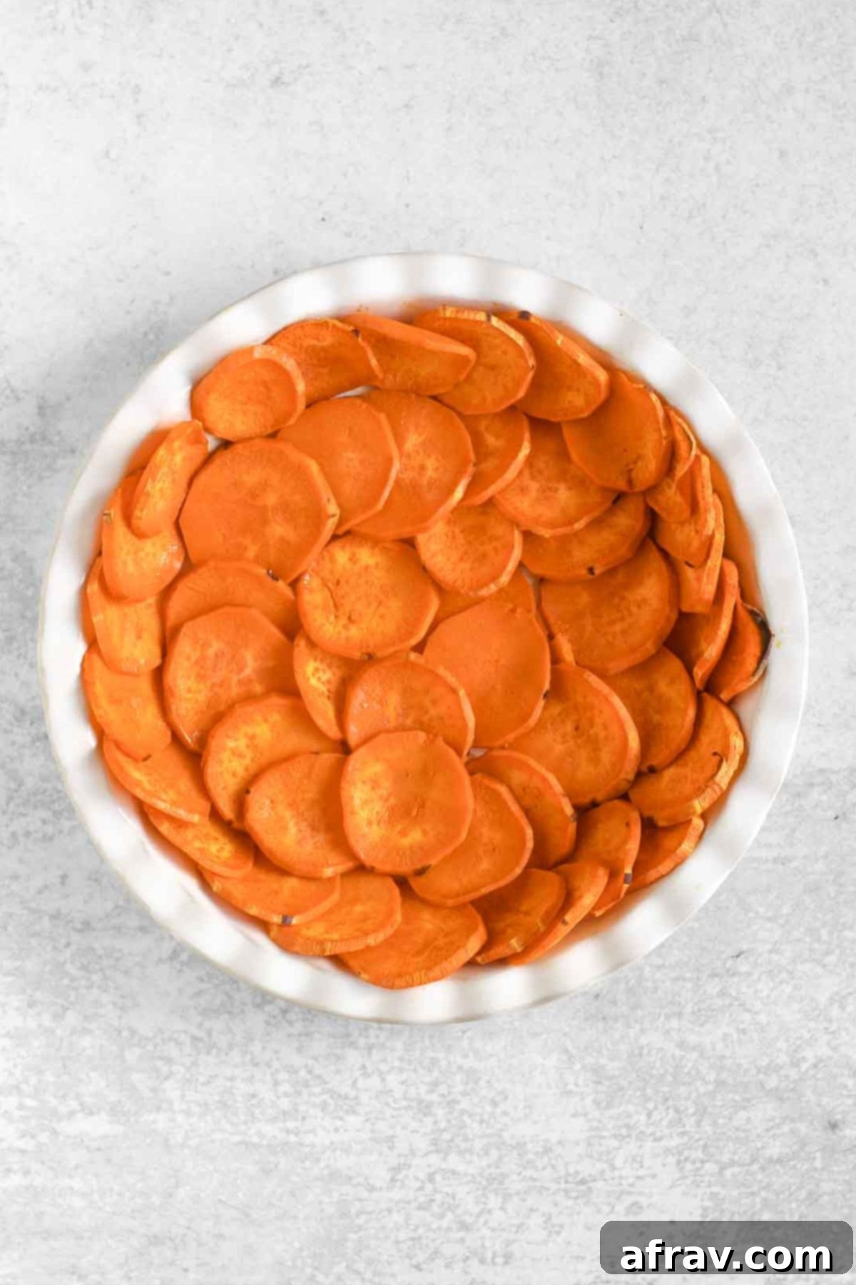 Baked sweet potato slices forming a golden brown crust in a white ceramic pie dish, lightly crisped at the edges.