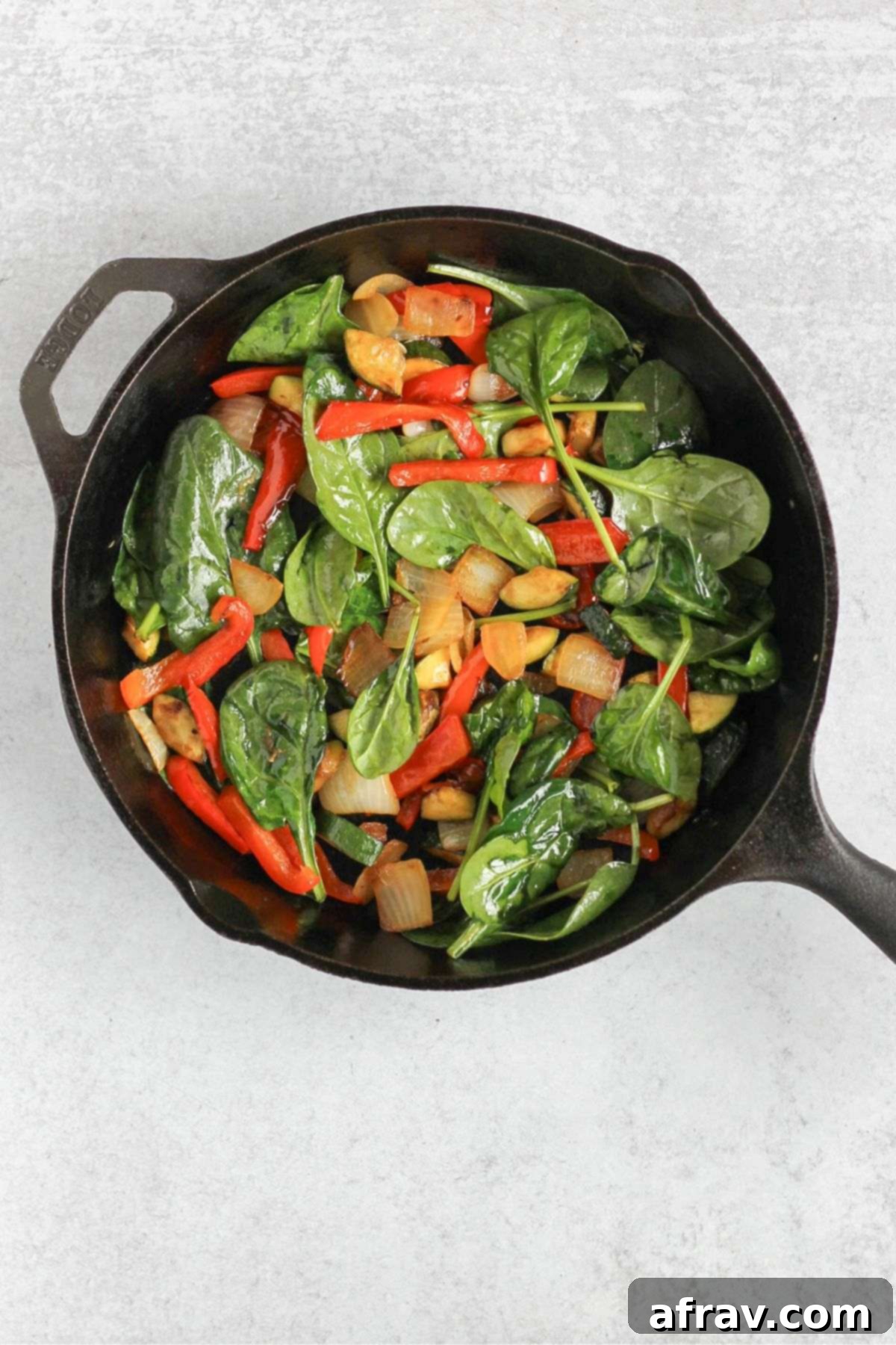 Wilted spinach mixed with other sautéed vegetables (peppers, zucchini, onion) in a cast iron skillet, ready for the quiche.