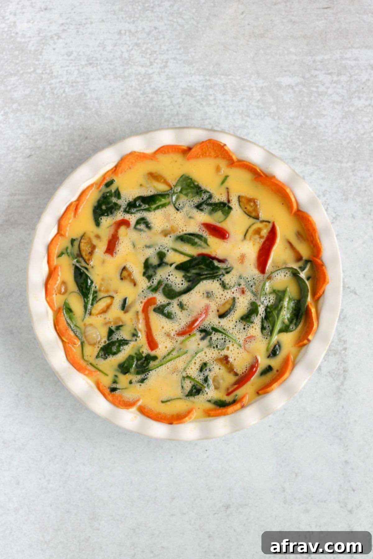 The pre-baked sweet potato crust in a pie dish, filled with sautéed vegetables, with the egg mixture poured over the top, ready for final baking.