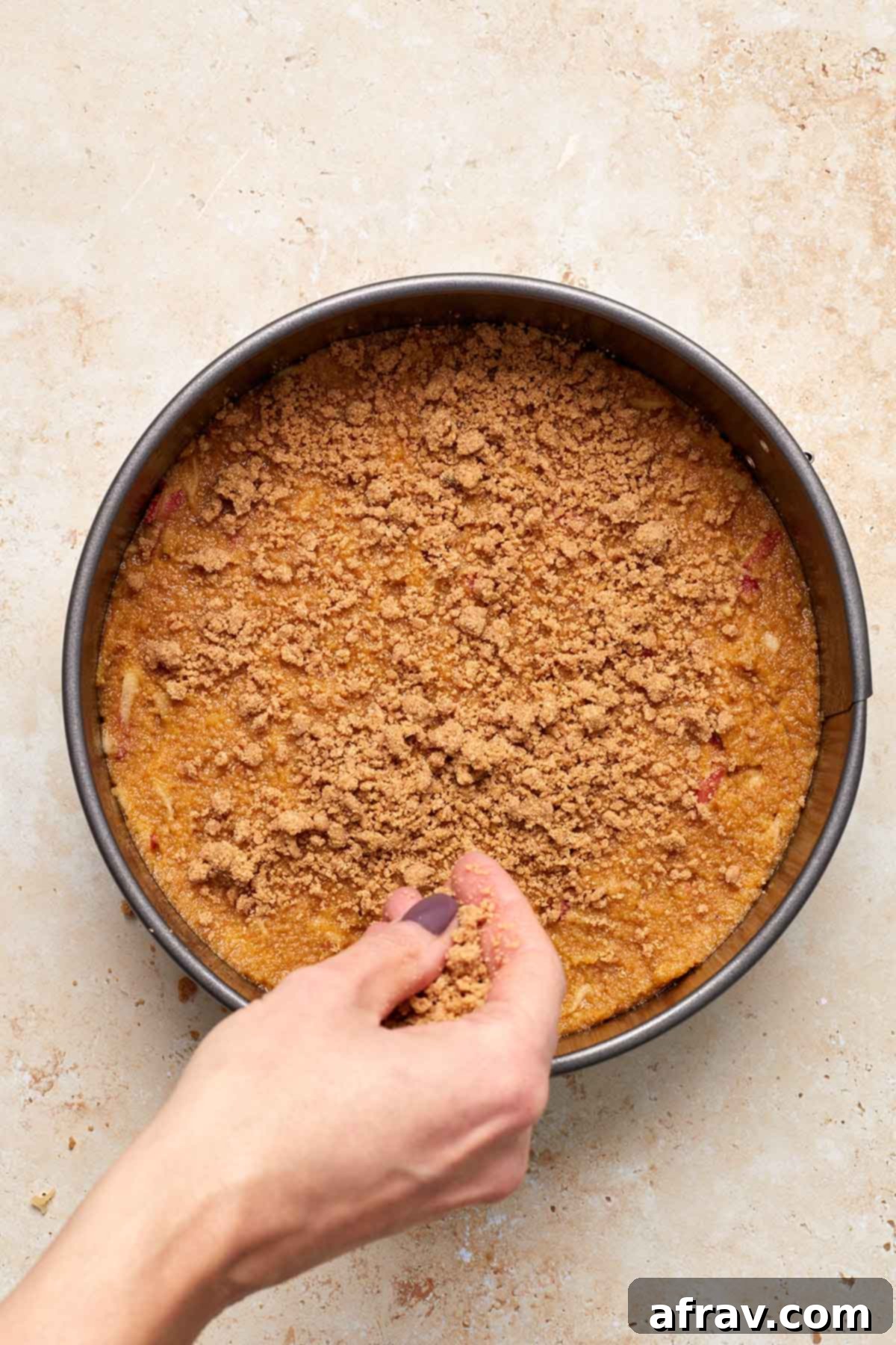 Delightful Almond Apple Cake 11 Streusel topping being scattered on top of cake batter in pan.