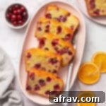 Slices of almond flour cranberry orange bread on a pink oval platter with orange slices and cranberries on the side, ready to be served.