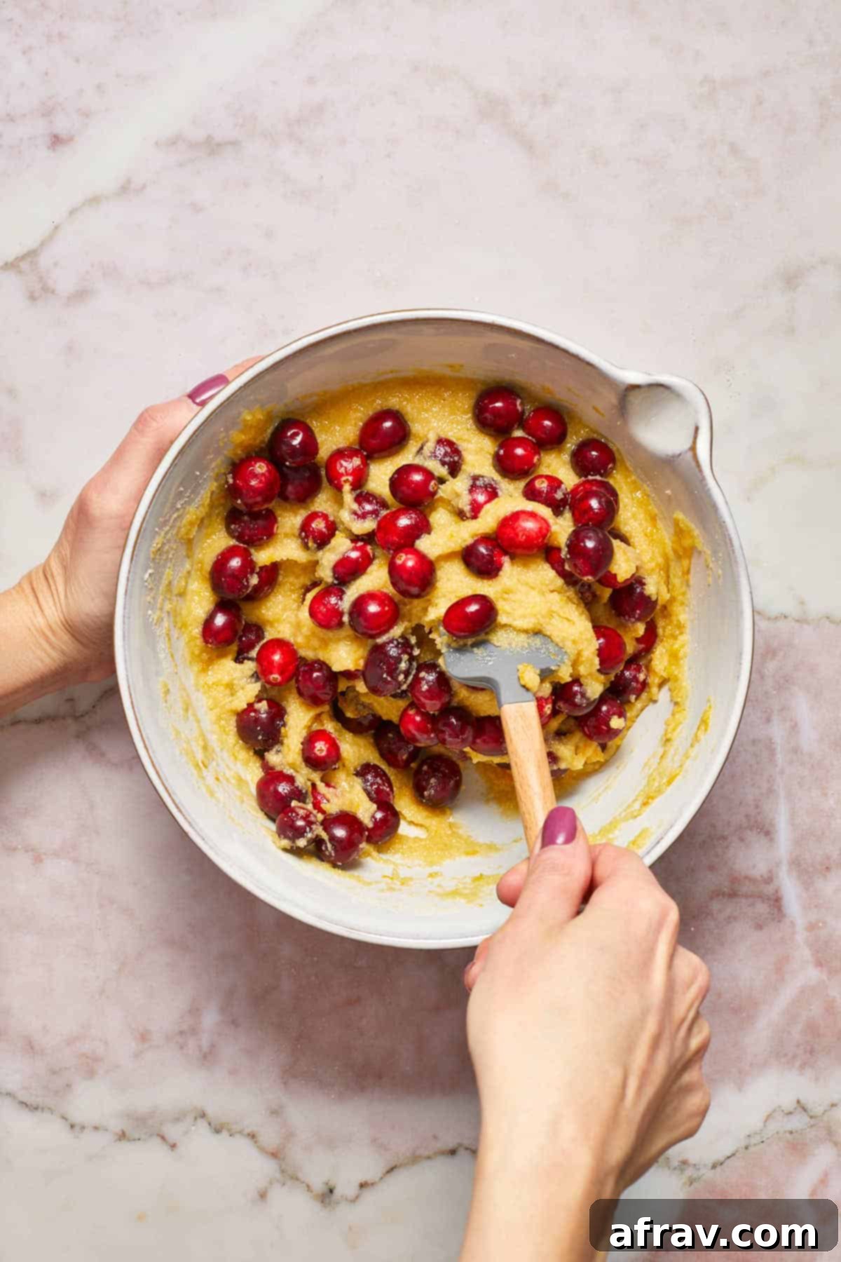 Fresh cranberries being gently stirred into the bread batter with a spatula.