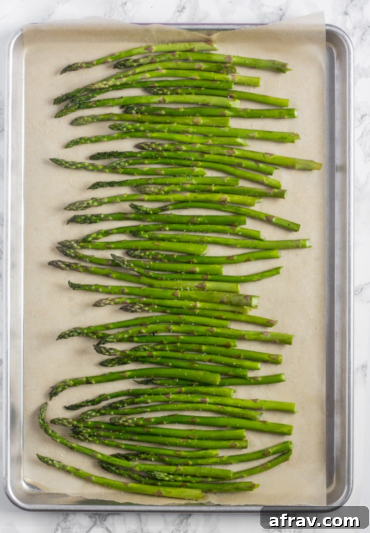 Easy Roasted Asparagus with Creamy Lemon Tahini Sauce 3 Raw asparagus spears neatly arranged on a baking sheet lined with parchment paper, ready for roasting.