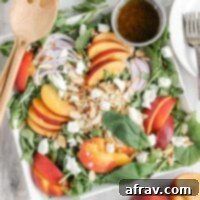 Peach and goat cheese salad with toasted almonds and sliced onions on a square plate with a side of balsamic vinaigrette.