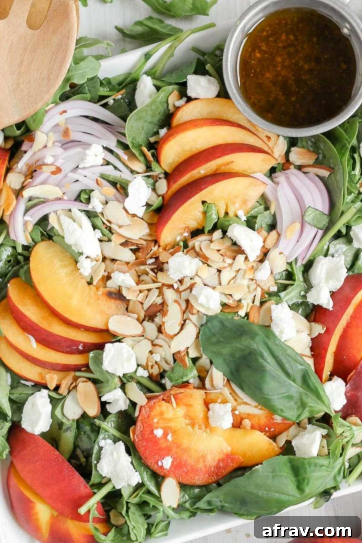 Mixed greens topped with sliced peaches, slivered almonds, red onion slices, goat cheese crumbles with a side of vinaigrette dressing, arranged beautifully on a plate.