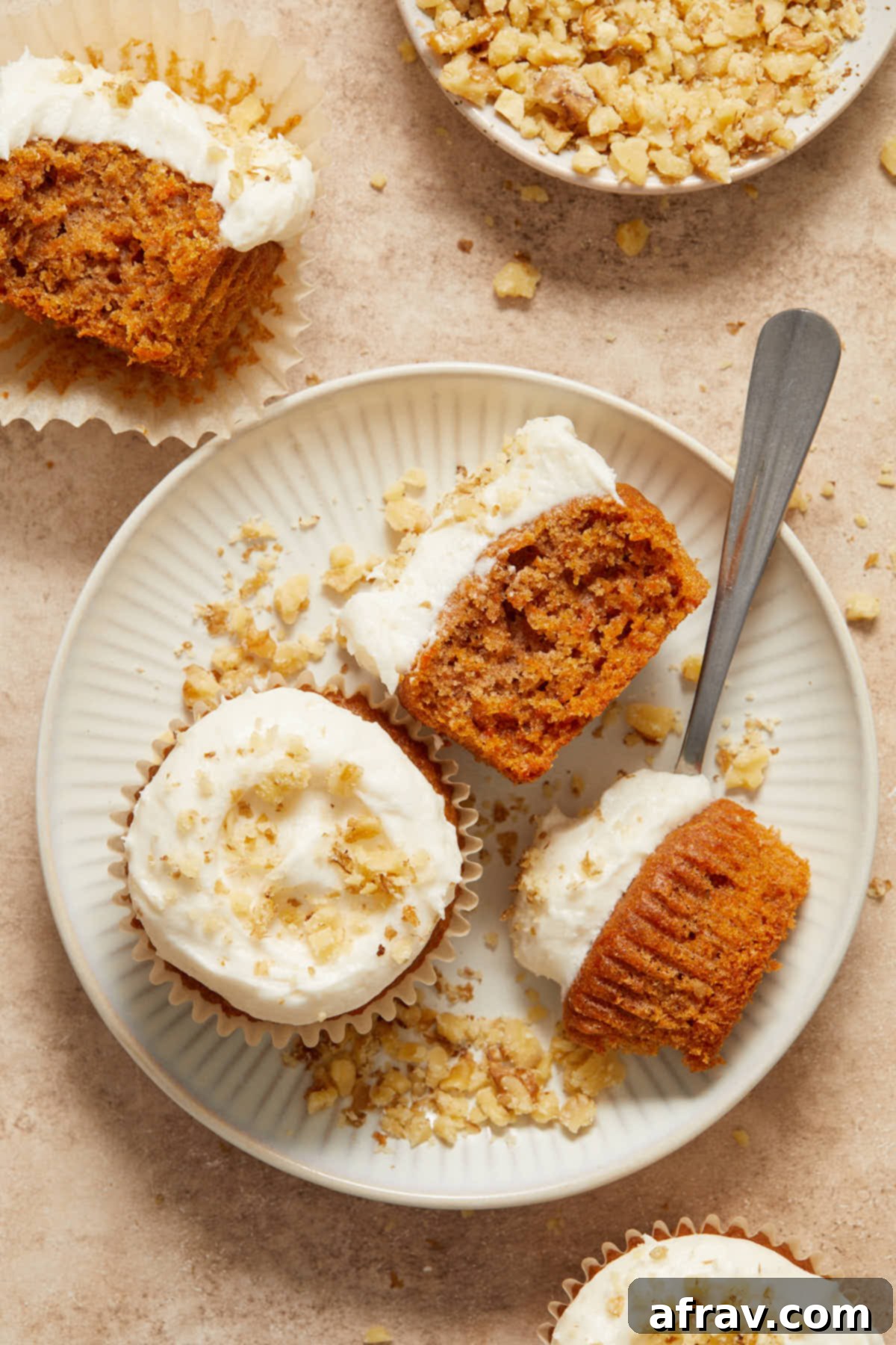 Scrumptious Gluten-Free Carrot Cake Delights 13 A plate of two frosted carrot cake cupcakes, with a fork gently pulling a piece from one, showcasing its tender texture.