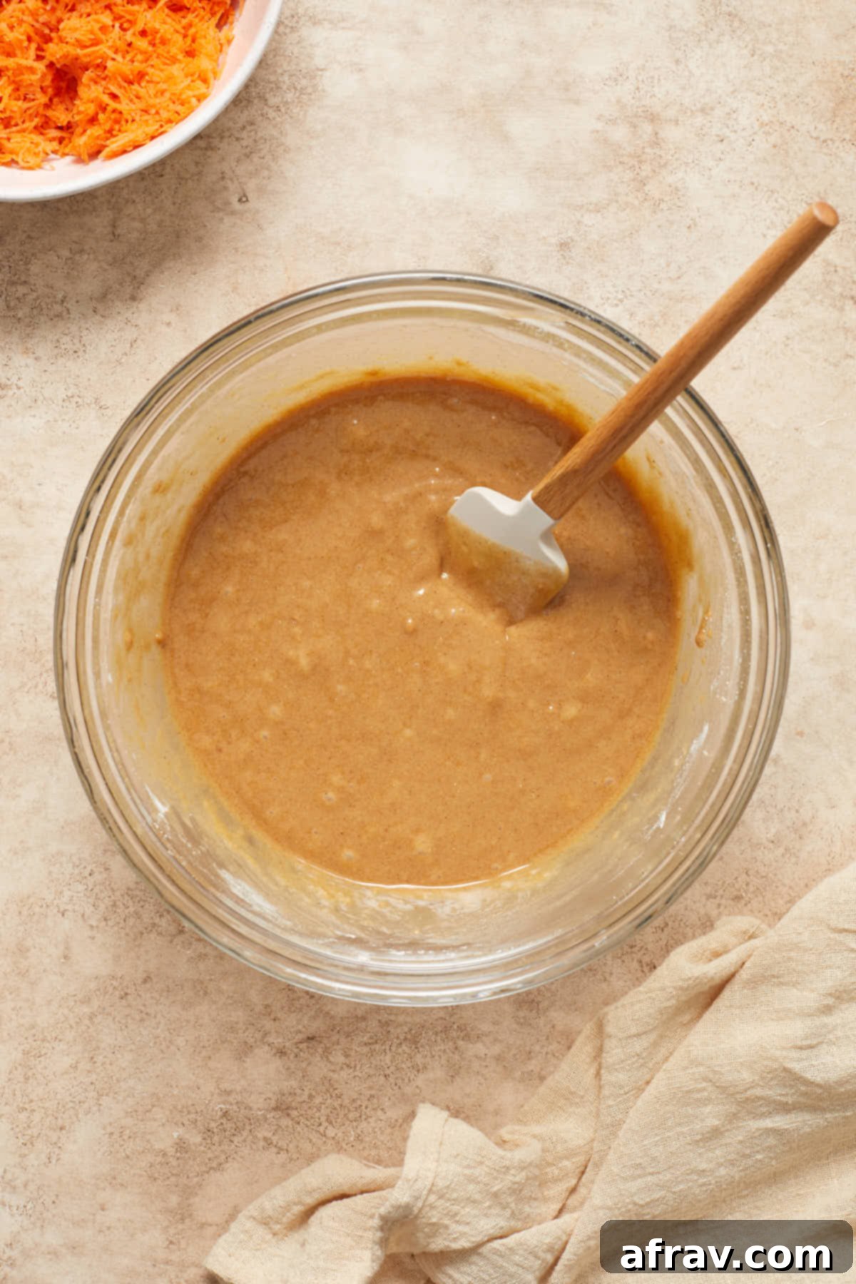 Scrumptious Gluten-Free Carrot Cake Delights 5 Cupcake batter in a glass bowl, with a spatula gently folding the dry ingredients into the wet mixture, ensuring it's just combined.