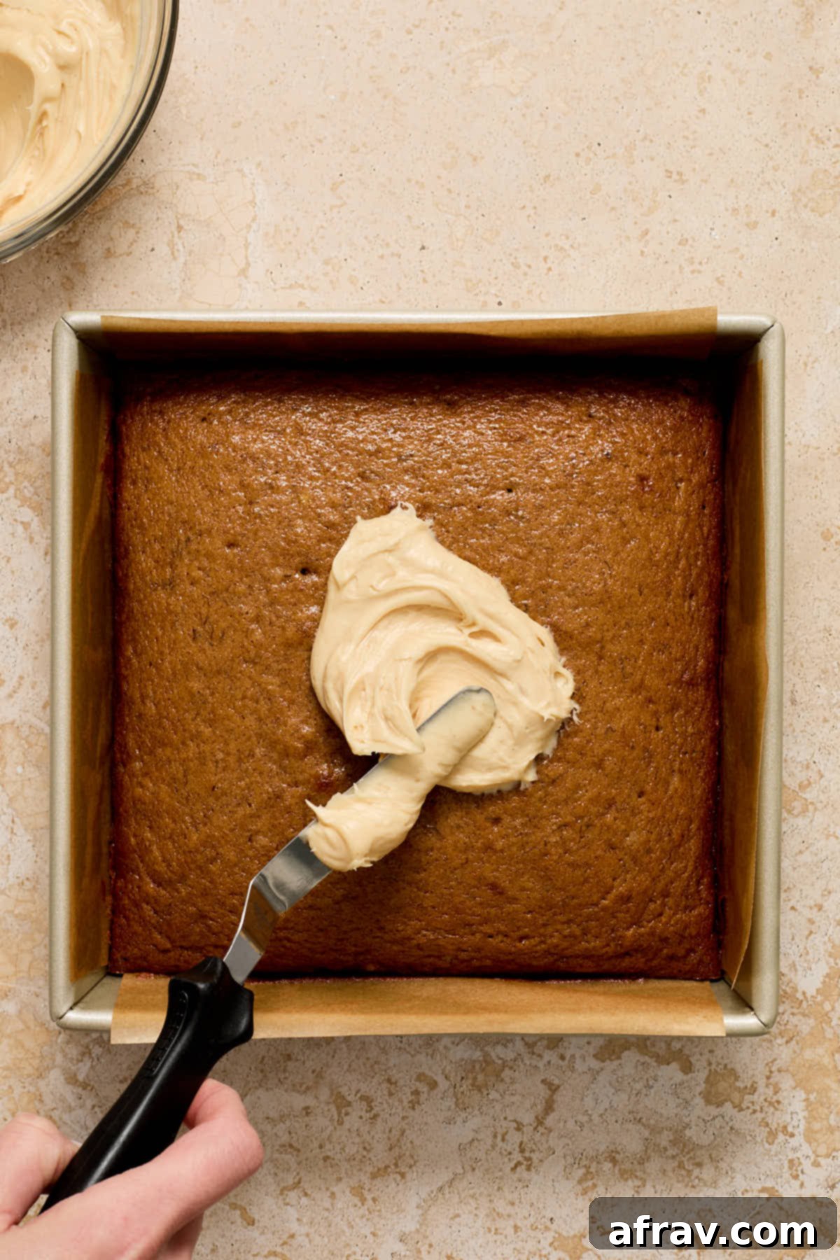Frosting being expertly spread onto a cooled banana cake with an offset spatula.