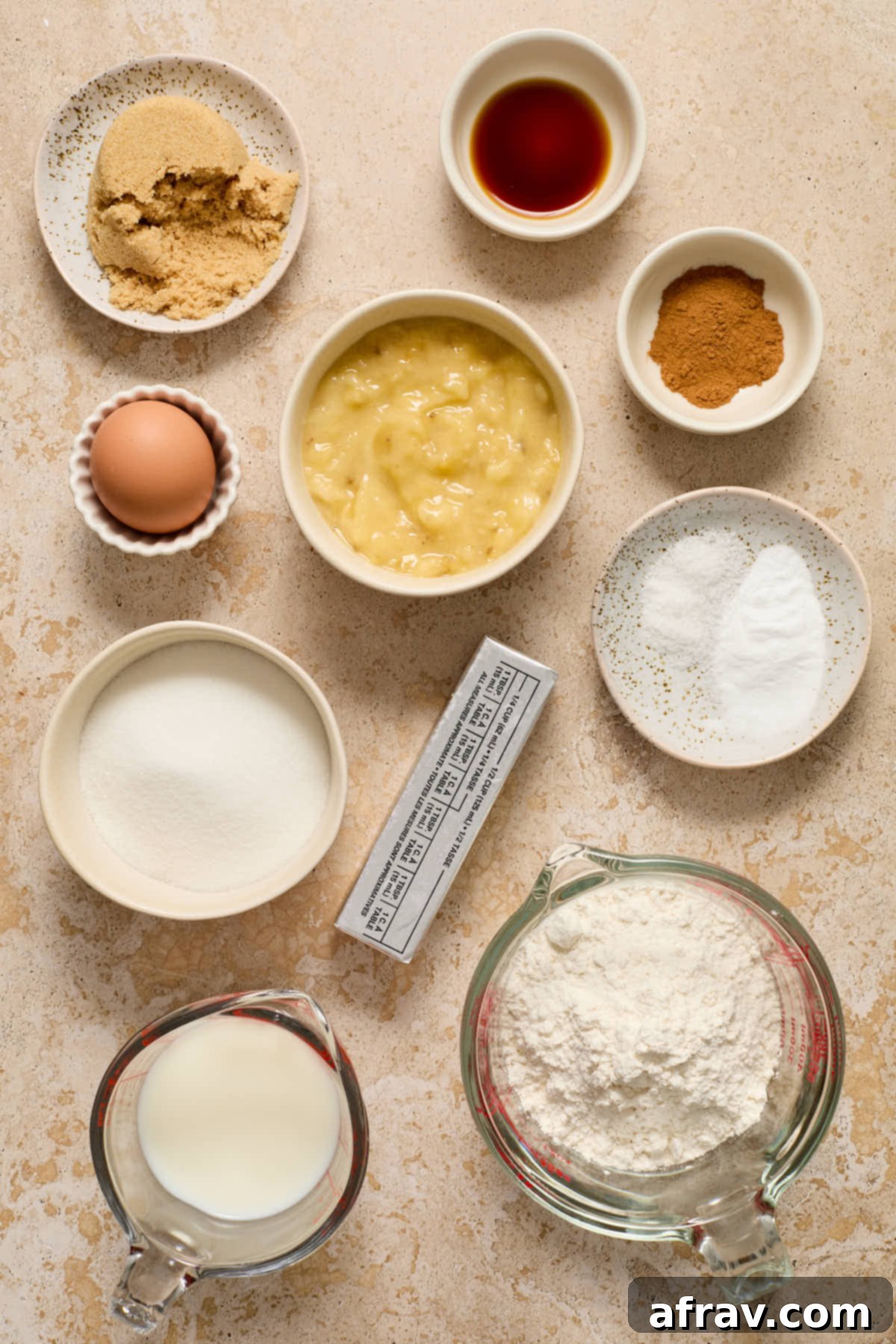 Various ingredients for banana cake laid out in individual bowls, including bananas, milk, butter, and flour.
