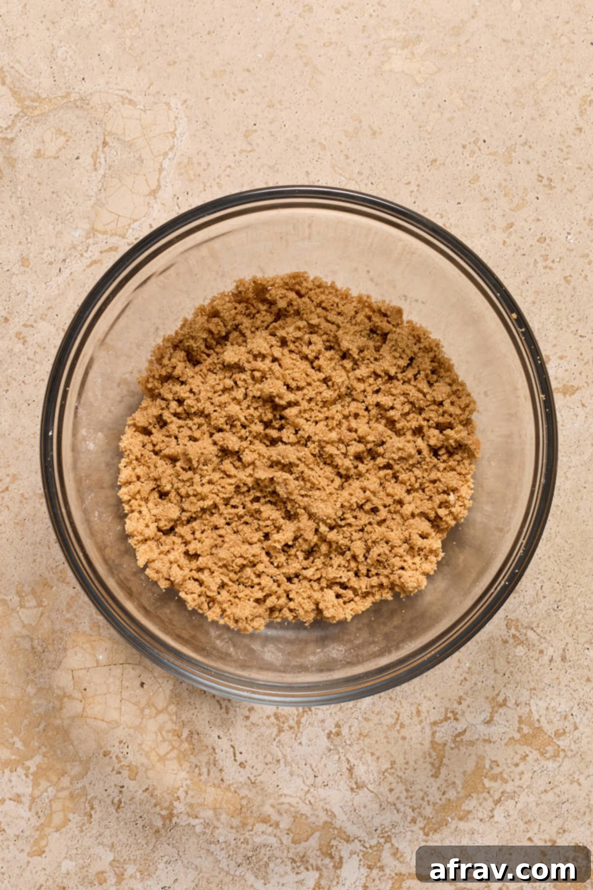 Close-up of streusel topping ingredients mixed together in a clear glass bowl, showing a crumbly texture.