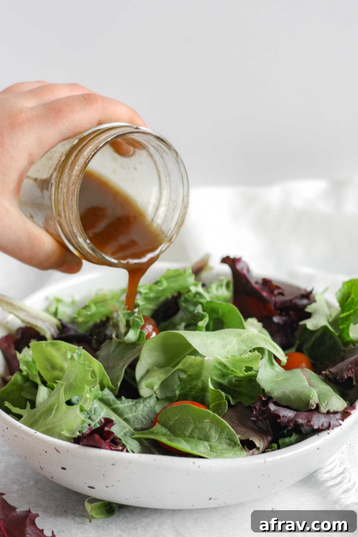 Effortless Balsamic Vinaigrette 2 Balsamic vinaigrette being poured over a bowl of mixed greens.