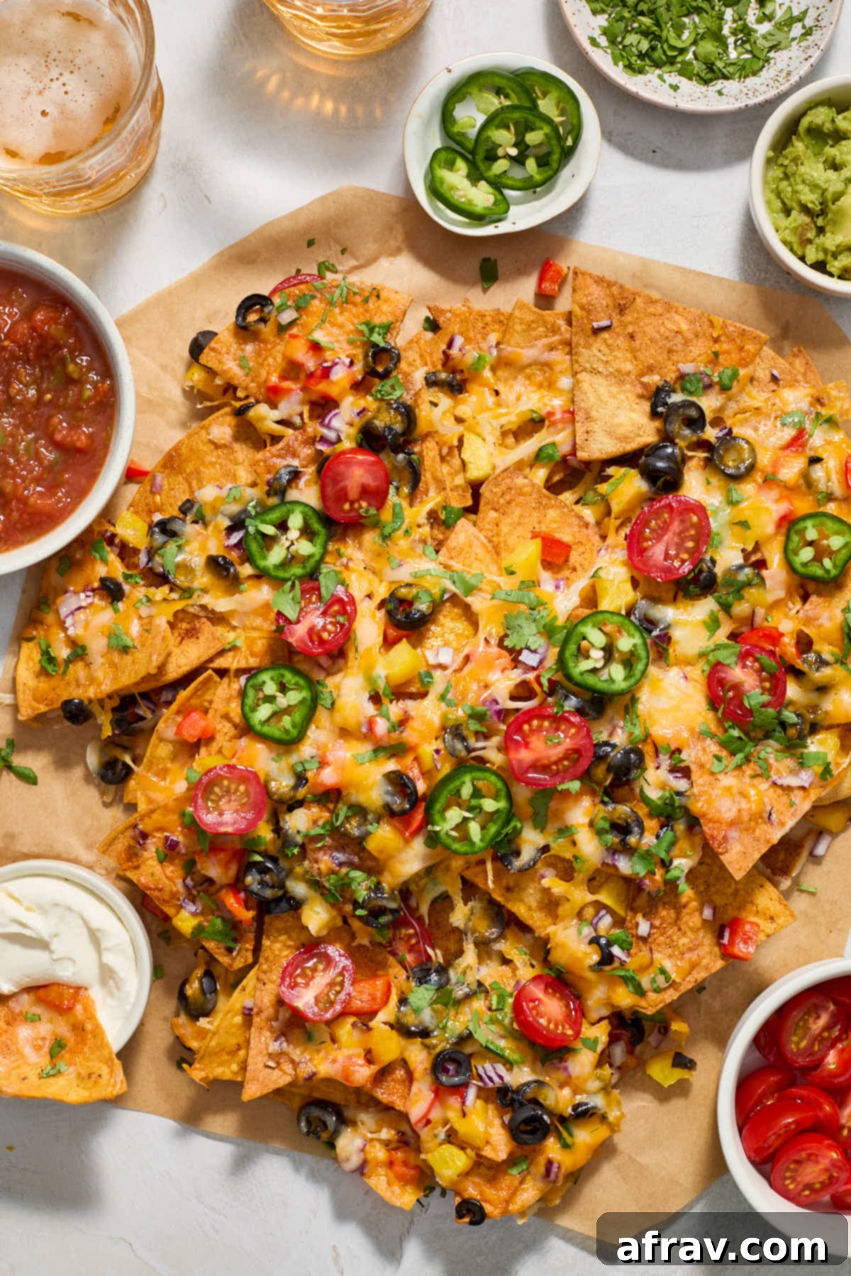 Air fryer nachos on brown parchment paper and surrounded by salsa, sour cream, guacamole, chopped tomatoes, cilantro and jalapenos.