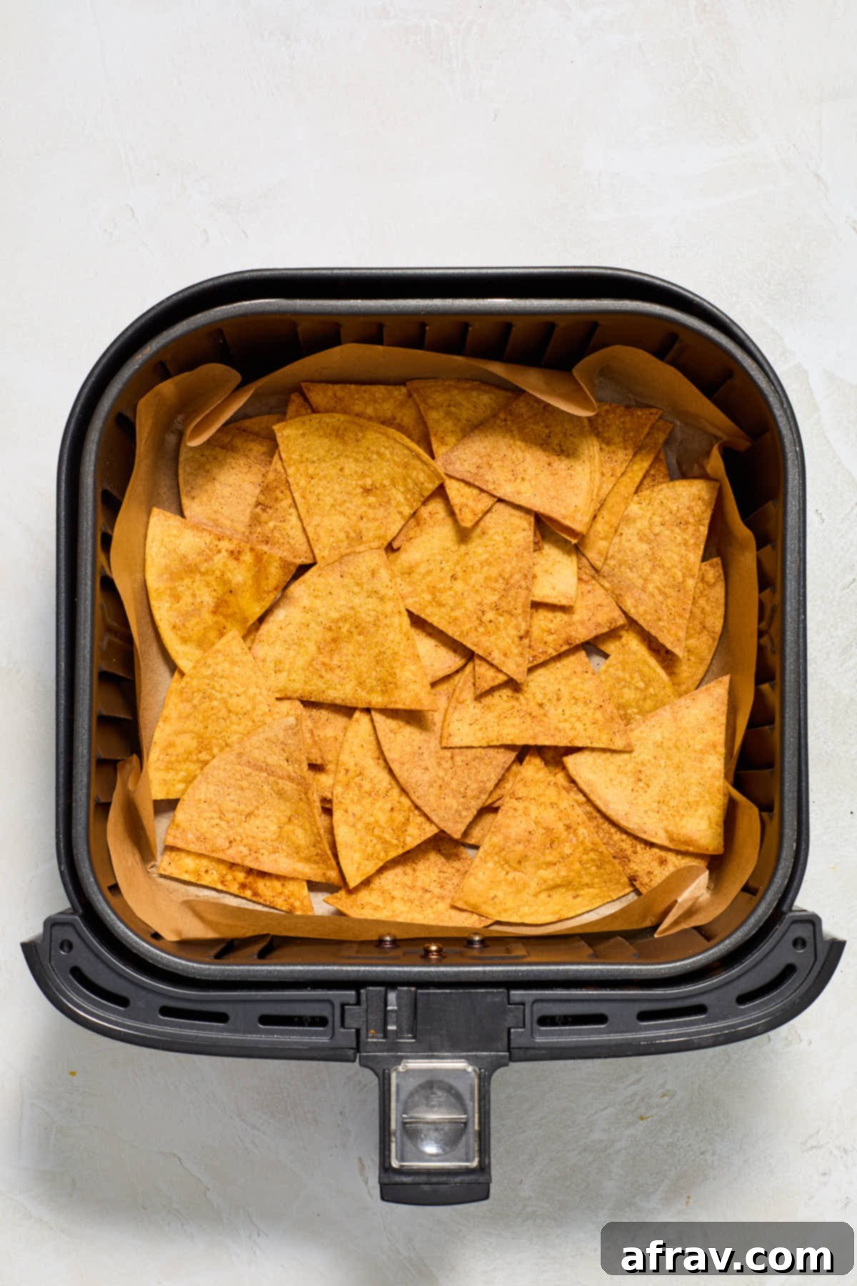 Layer of tortilla chips arranged on the bottom of a parchment paper lined air fryer basket.