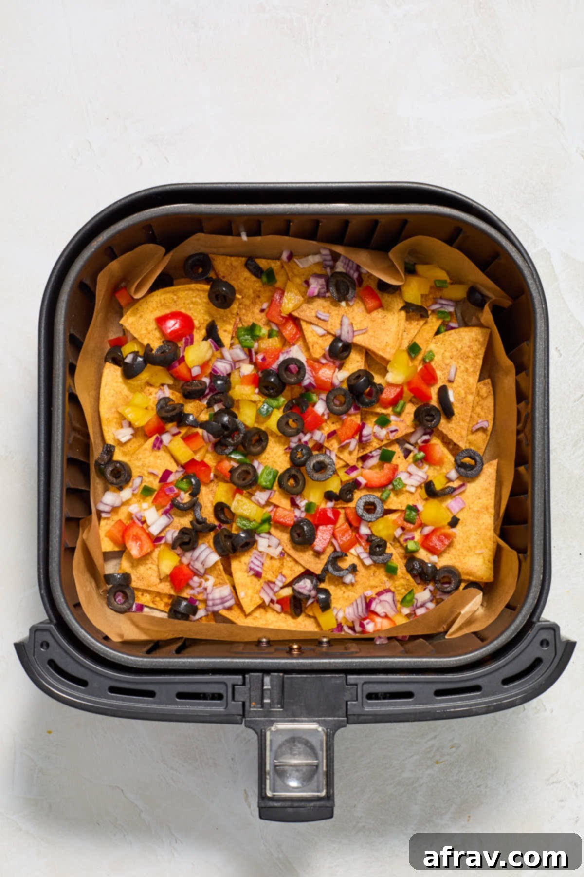 Chopped peppers, onions and black olives layered on top of the tortilla chips in the air fryer basket.