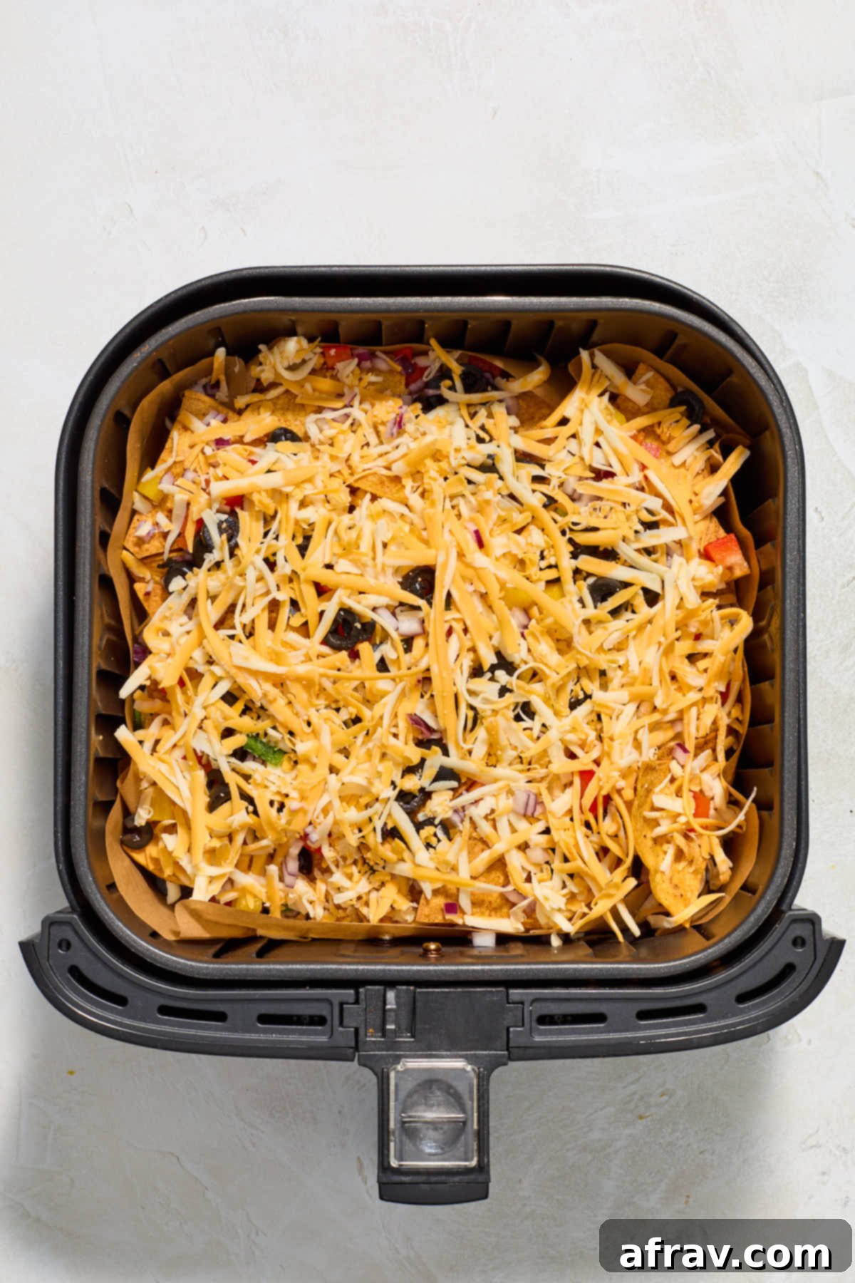 Grated cheese added to the top of the nacho layers in the air fryer basket.