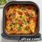 Air fried nachos in the air fryer basket and topped with cherry tomatoes and chopped cilantro.