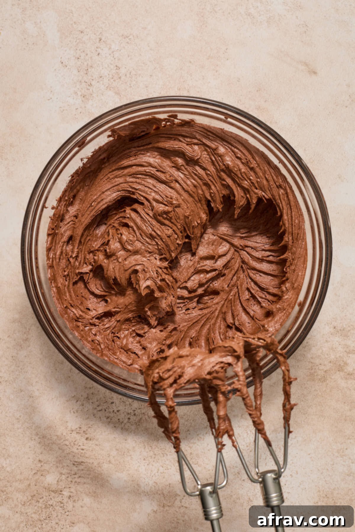 Buttercream frosting being whipped together in a glass bowl with handheld beaters, showing the creamy texture forming.