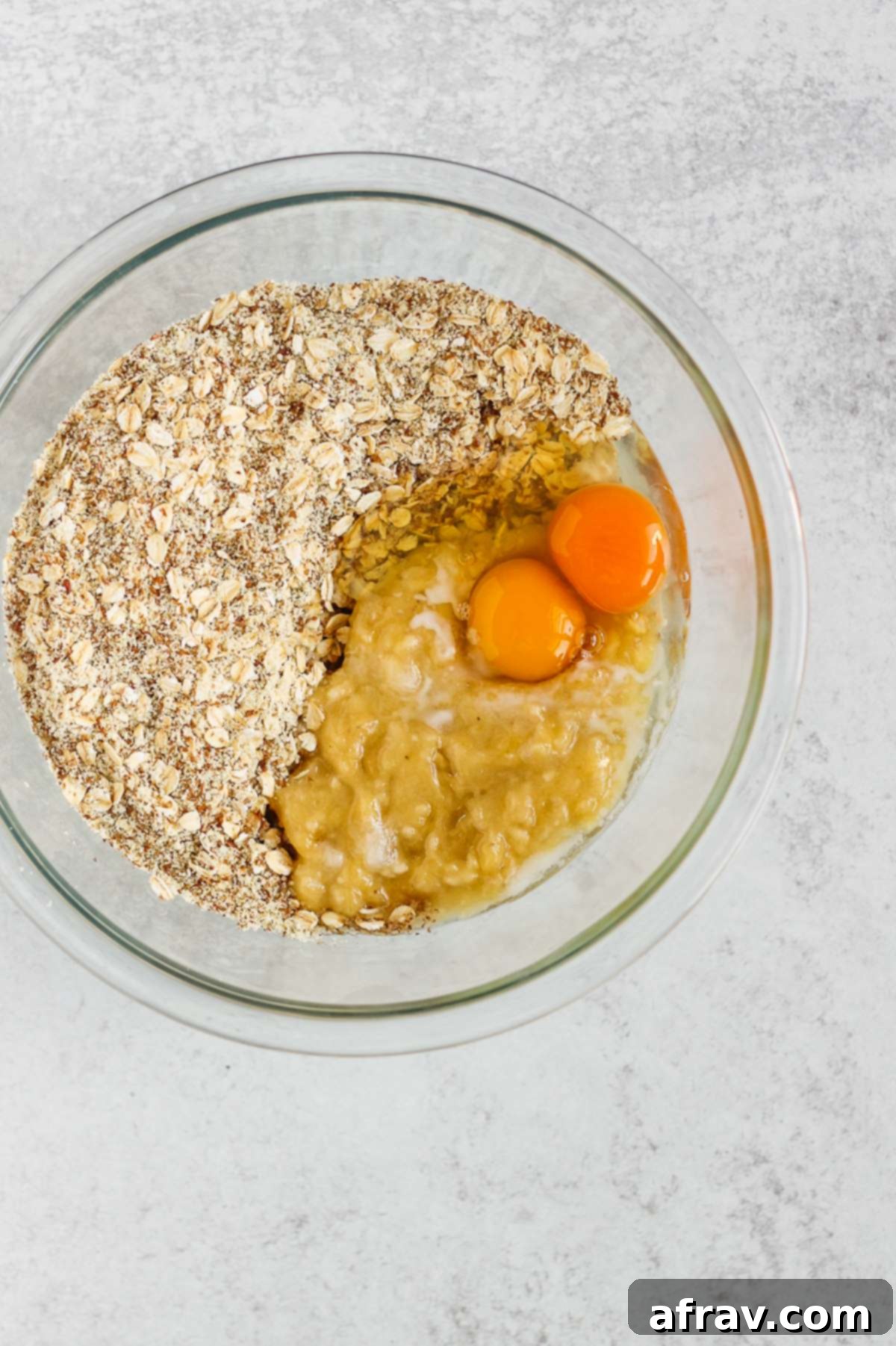 Mixing bowl with oats and almond flour on one side and eggs and mashed banana on the other side, illustrating the one-bowl method.
