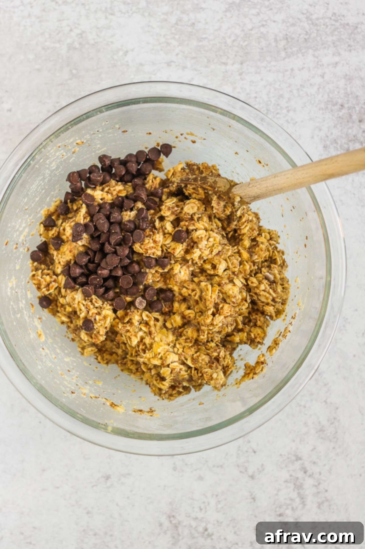 Oat mixture in a mixing bowl with chocolate chips and a wooden mixing spoon, ready to be formed.