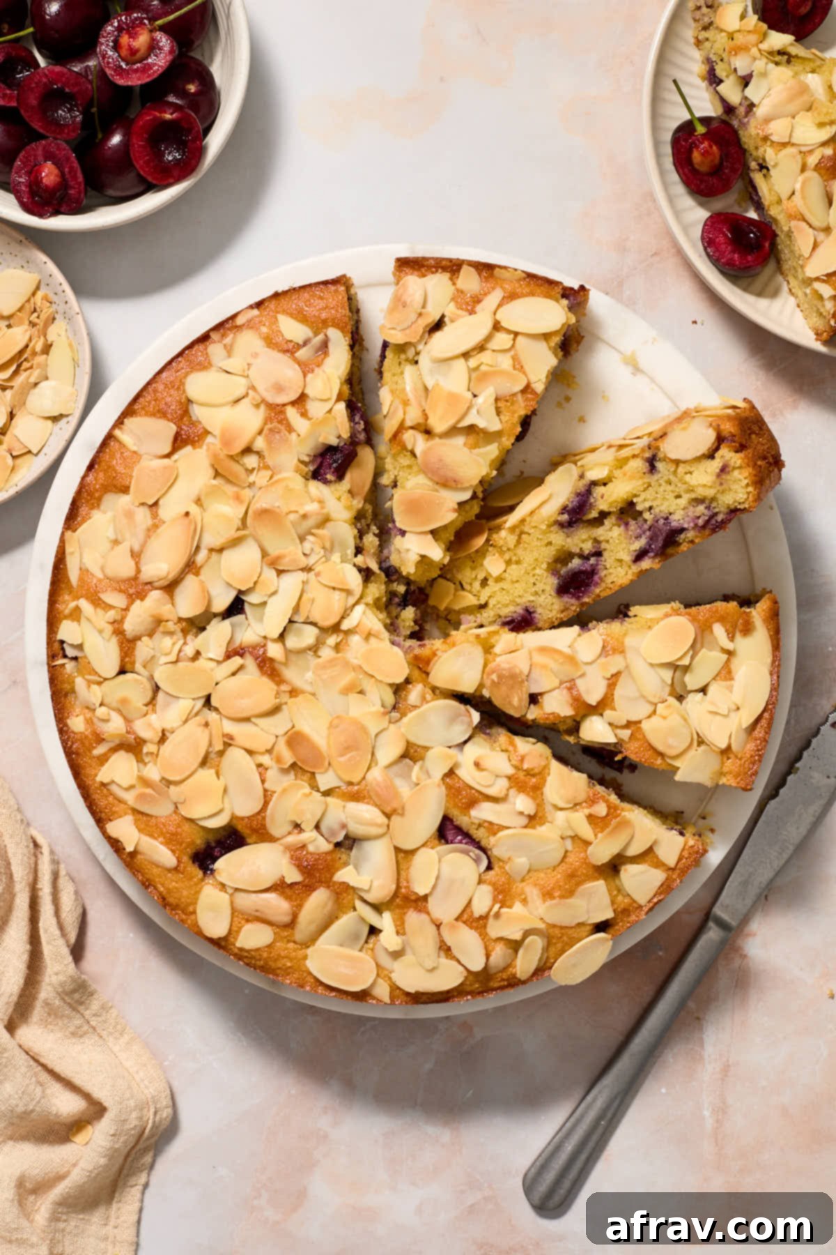 Cake partially sliced with bowls of cherries and almonds on the side.